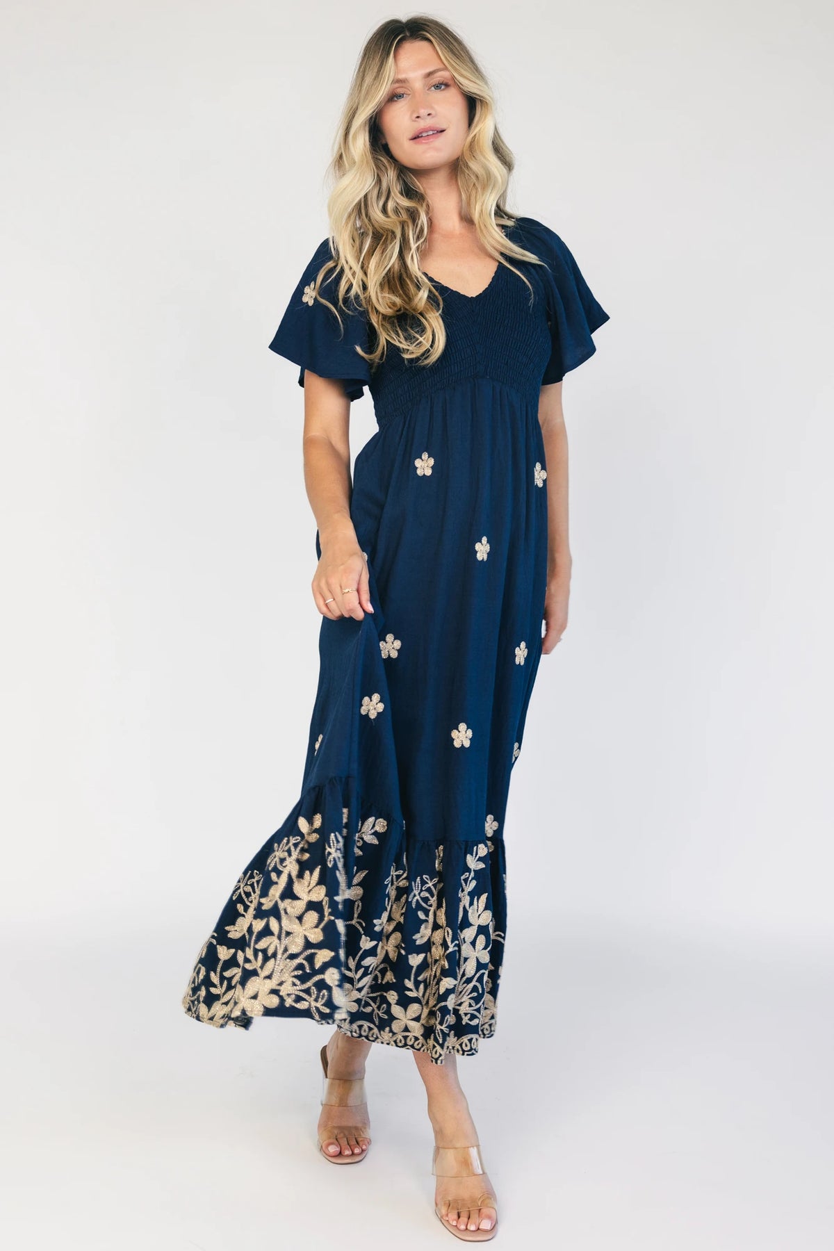 Model wearing a navy embroidered maxi dress with a V-neckline, flutter sleeves, and a smocked bodice.