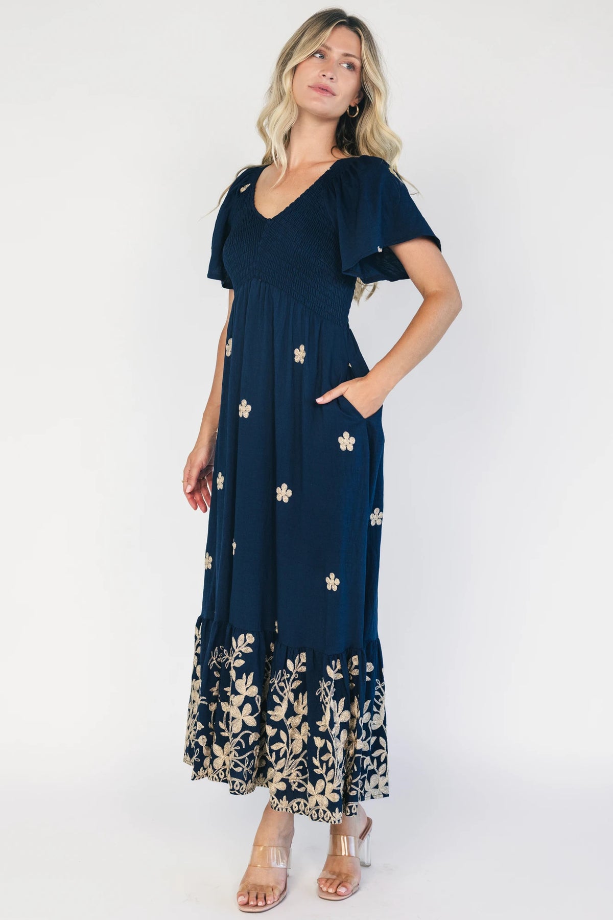 Model wearing a navy embroidered maxi dress with a V-neckline, flutter sleeves, and a smocked bodice.