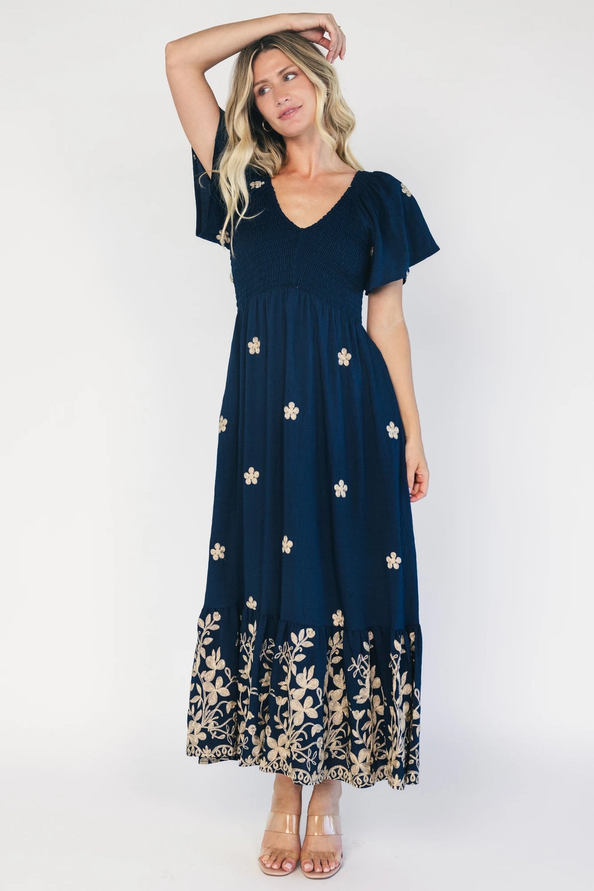 Model wearing a navy embroidered maxi dress with a V-neckline, flutter sleeves, and a smocked bodice.
