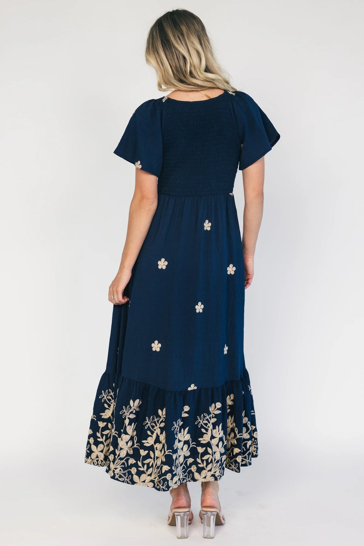 Model wearing a navy embroidered maxi dress with a V-neckline, flutter sleeves, and a smocked bodice.