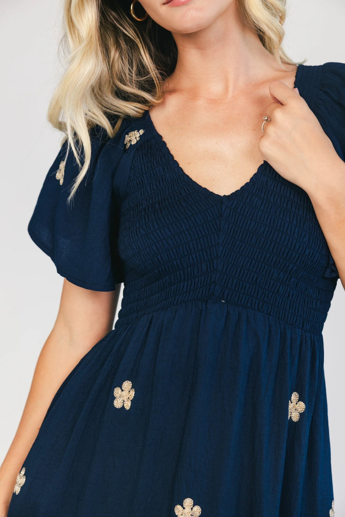 Model wearing a navy embroidered maxi dress with a V-neckline, flutter sleeves, and a smocked bodice.