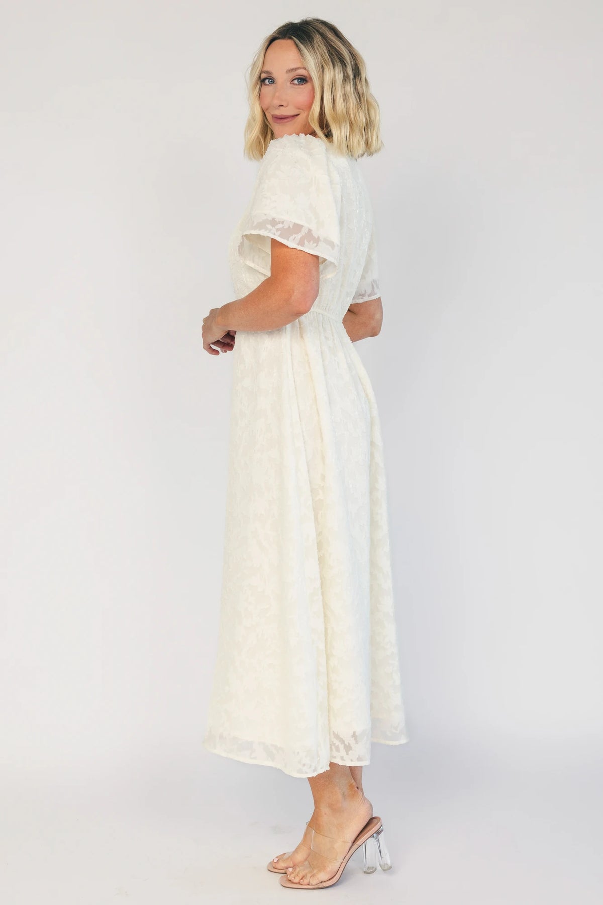 Model wearing a cream midi dress with a round neckline, short gathered sleeves, and a fitted bodice.