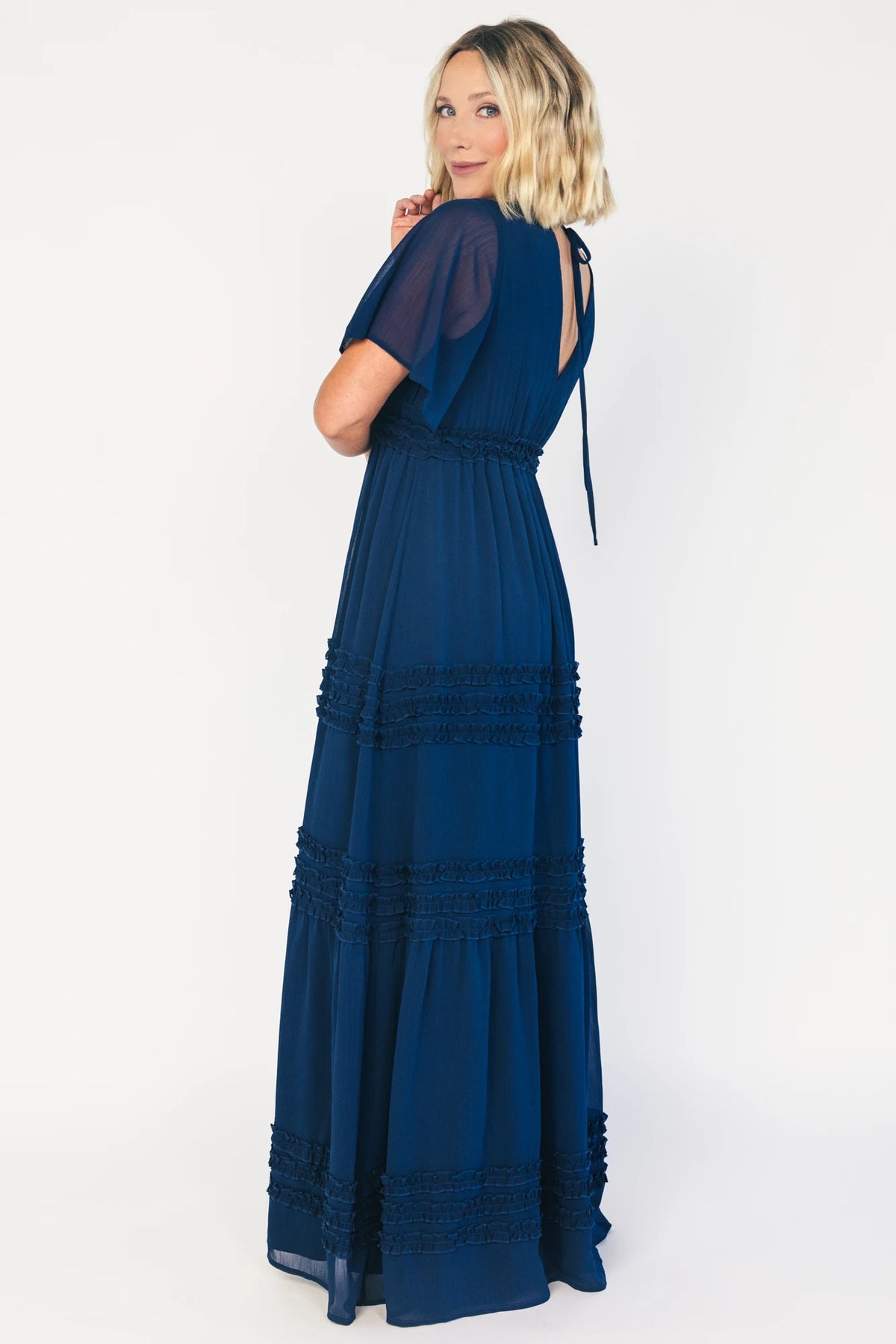 Model wearing a navy chiffon maxi dress with a surplice V-neckline, short ruffled sleeves, and an elastic empire waist.