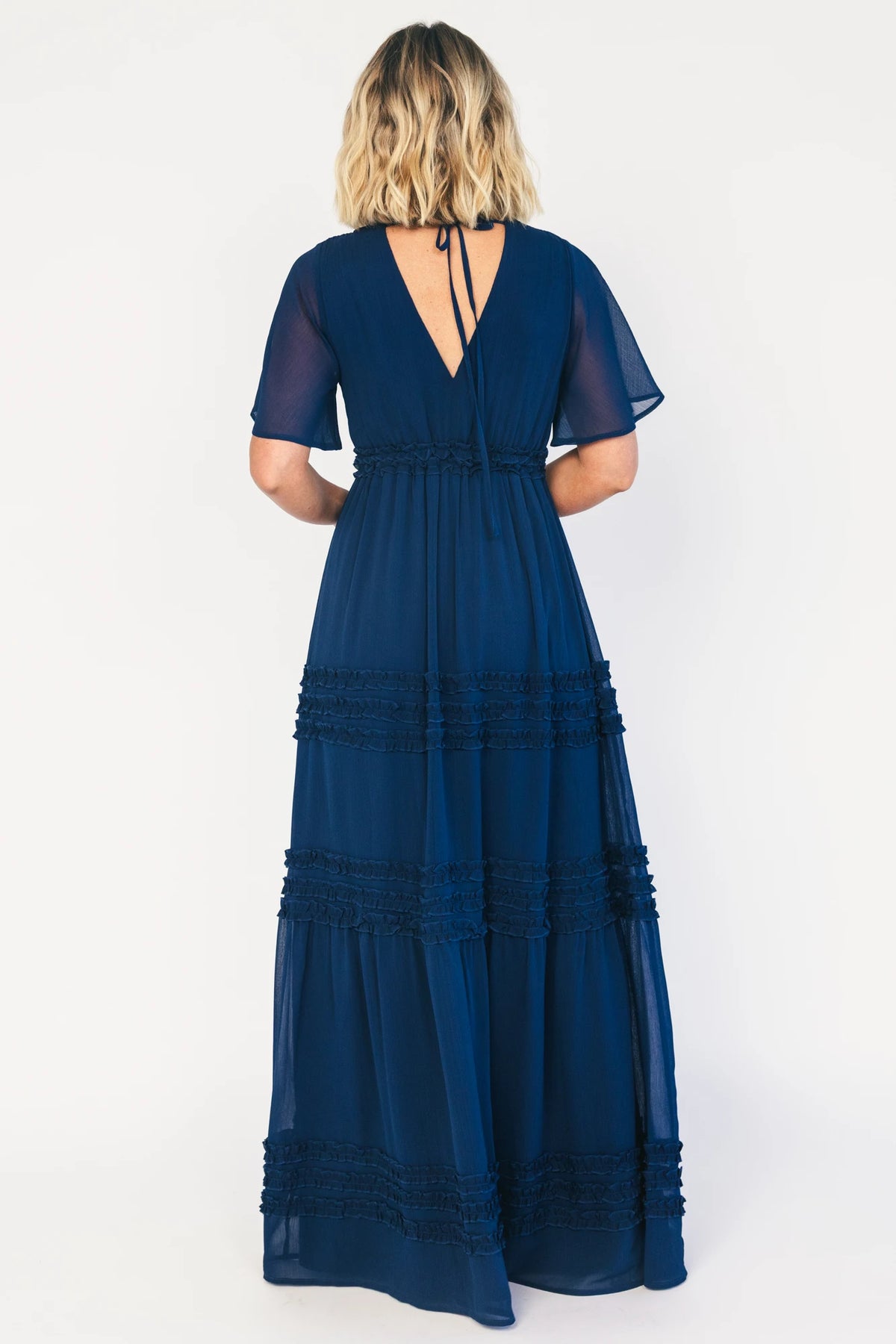 Model wearing a navy chiffon maxi dress with a surplice V-neckline, short ruffled sleeves, and an elastic empire waist.