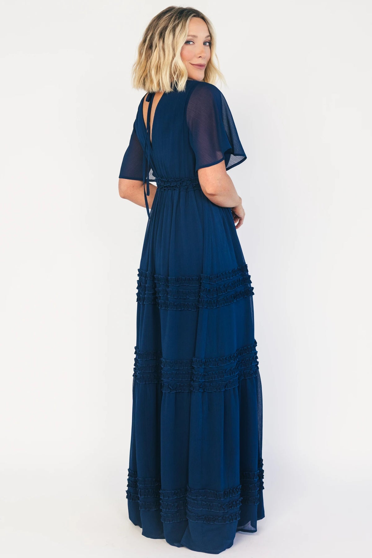 Model wearing a navy chiffon maxi dress with a surplice V-neckline, short ruffled sleeves, and an elastic empire waist.