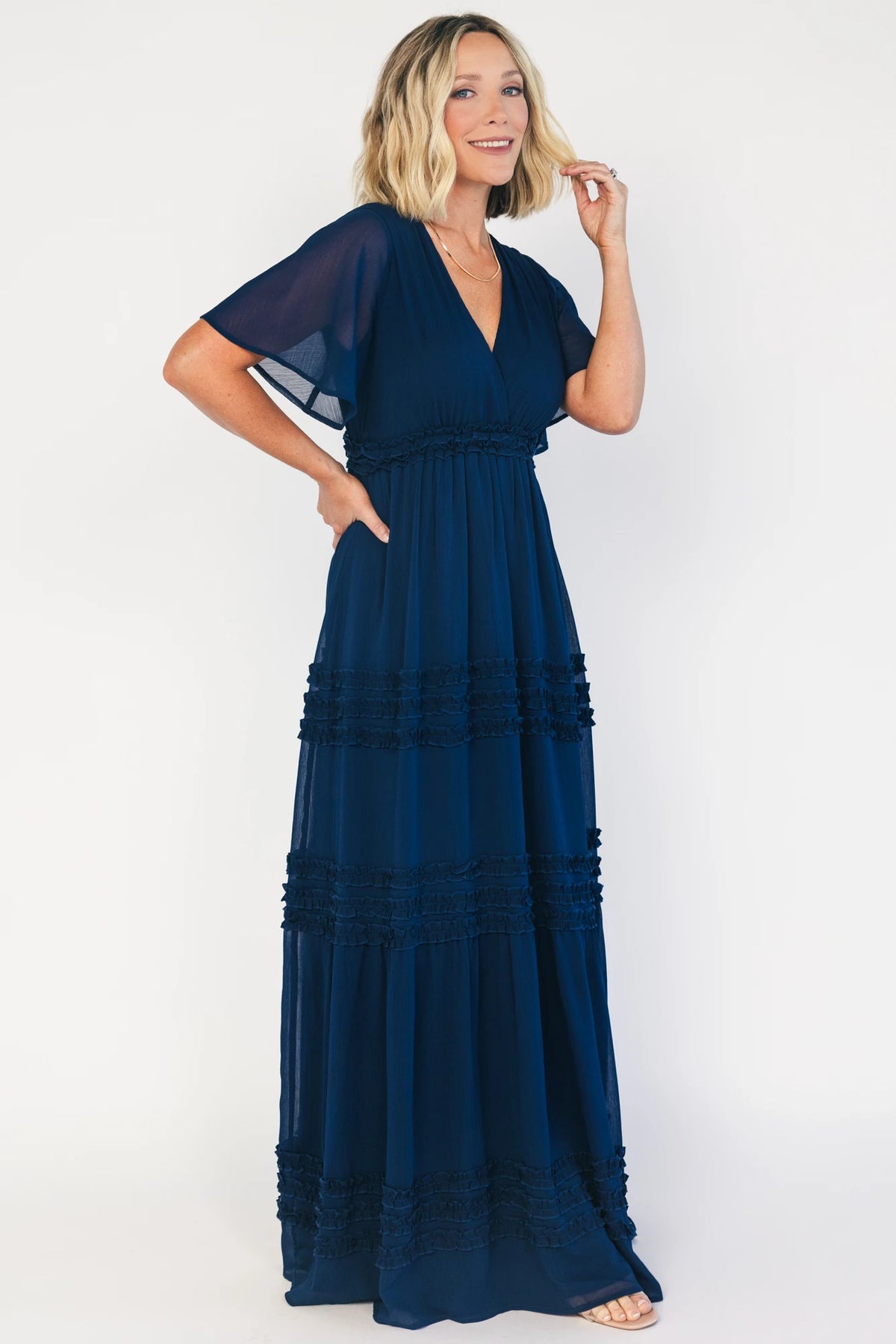 Model wearing a navy chiffon maxi dress with a surplice V-neckline, short ruffled sleeves, and an elastic empire waist.