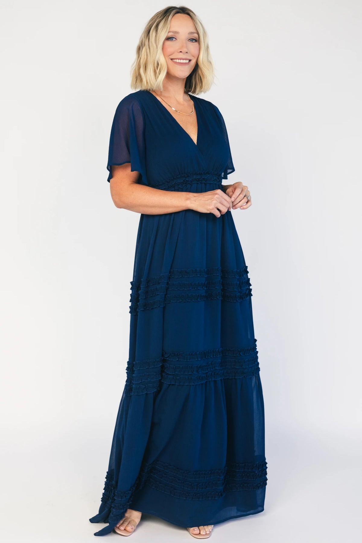 Model wearing a navy chiffon maxi dress with a surplice V-neckline, short ruffled sleeves, and an elastic empire waist.