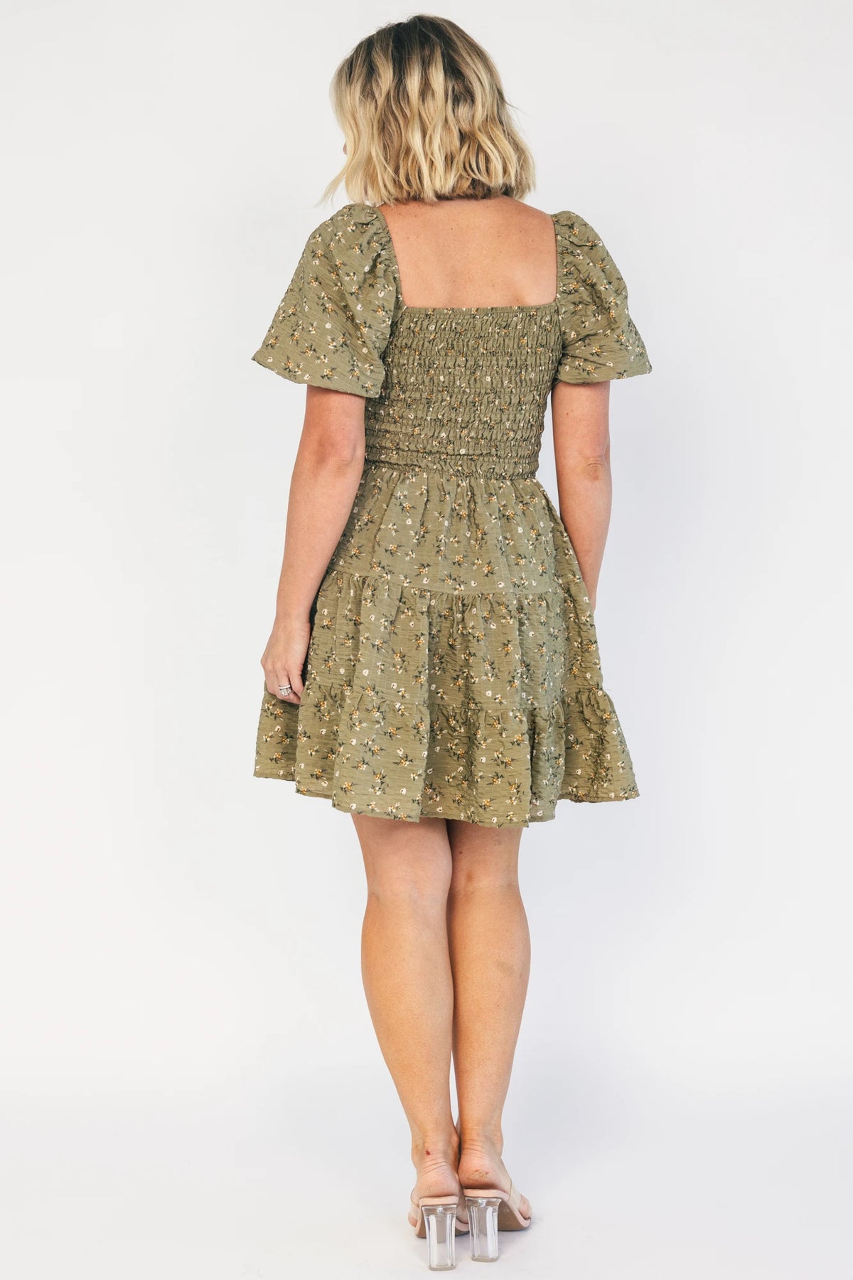 Model wearing an olive floral short dress with a square neckline, fully smocked bodice, and short balloon sleeves.