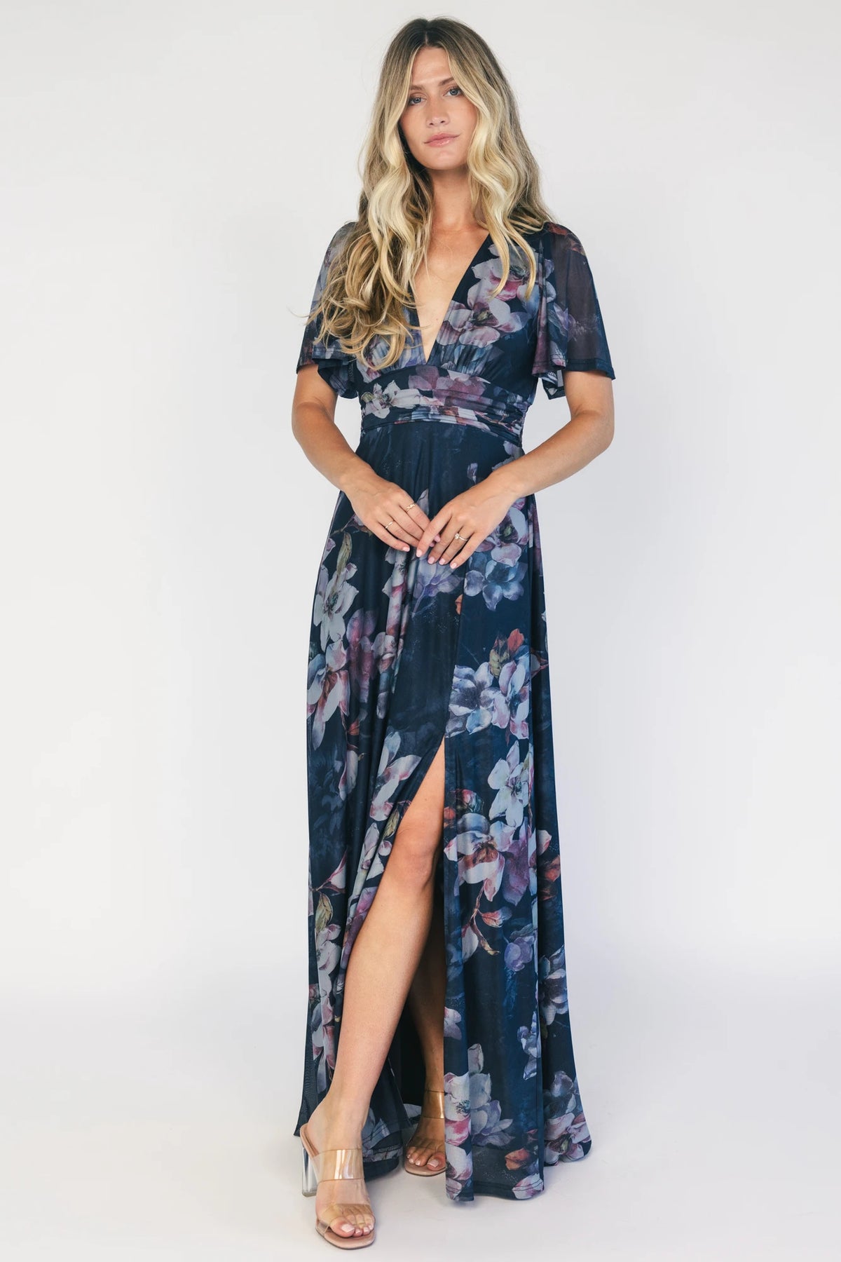 Model wearing a deep blue floral maxi dress with a deep V-neckline, short flutter sleeves, and an empire waist.