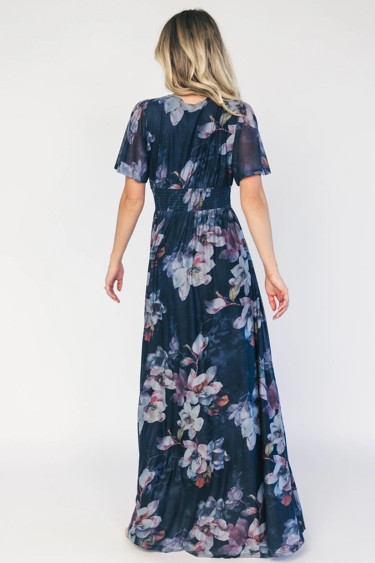 Model wearing a deep blue floral maxi dress with a deep V-neckline, short flutter sleeves, and an empire waist.