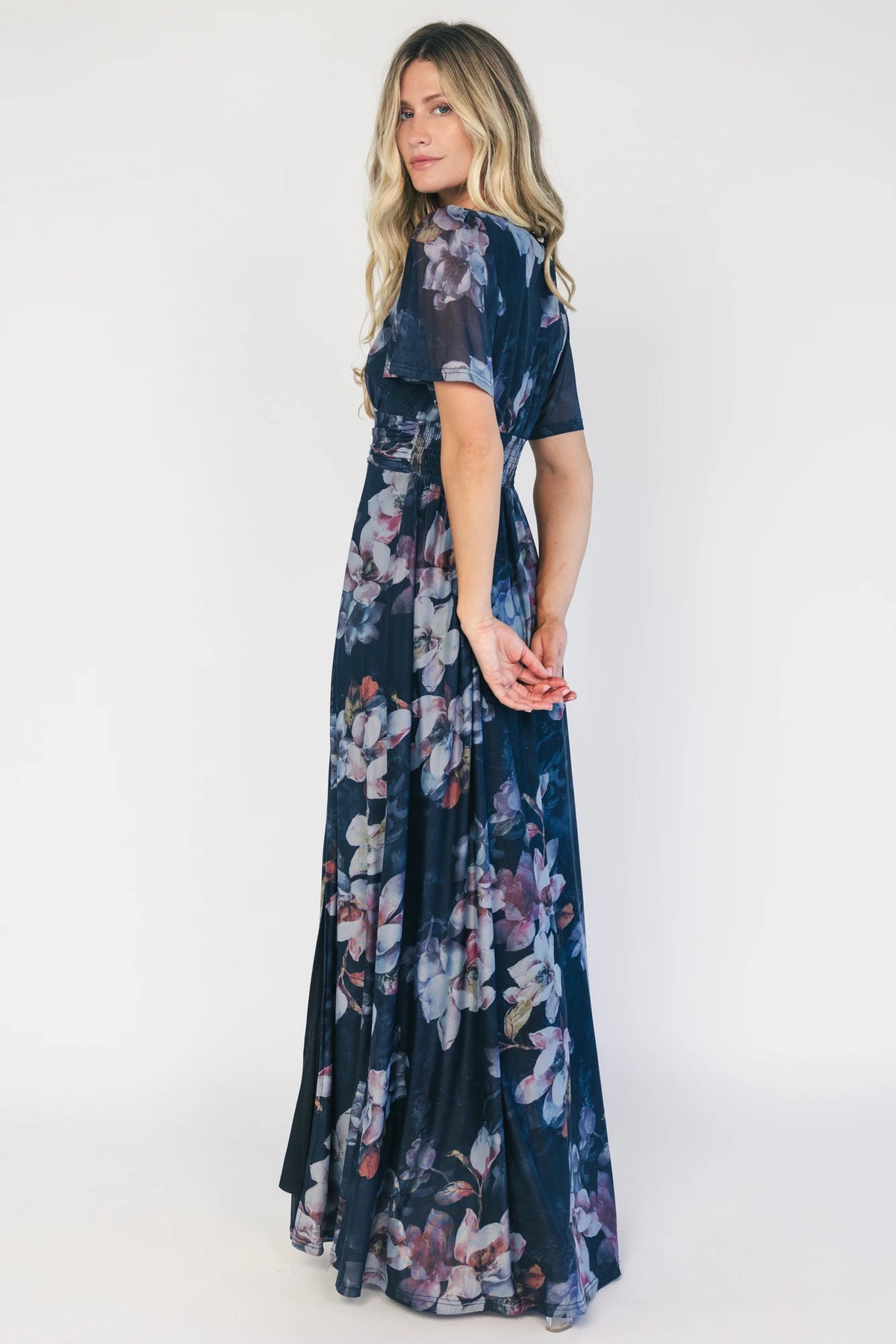 Model wearing a deep blue floral maxi dress with a deep V-neckline, short flutter sleeves, and an empire waist.