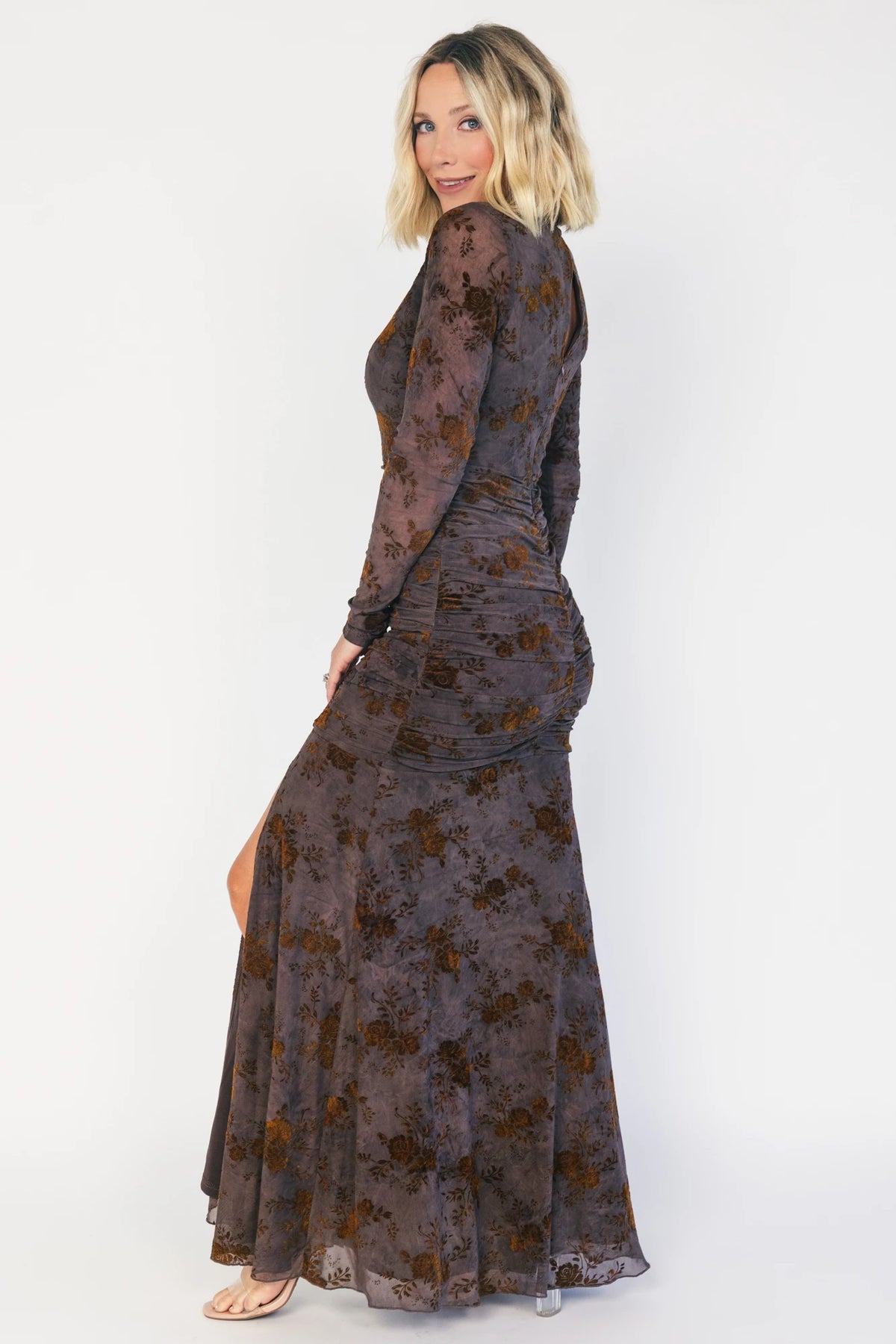 Model wearing a clove maxi dress with copper velvet burnout detailing, a high round neckline, and long sheer sleeves.