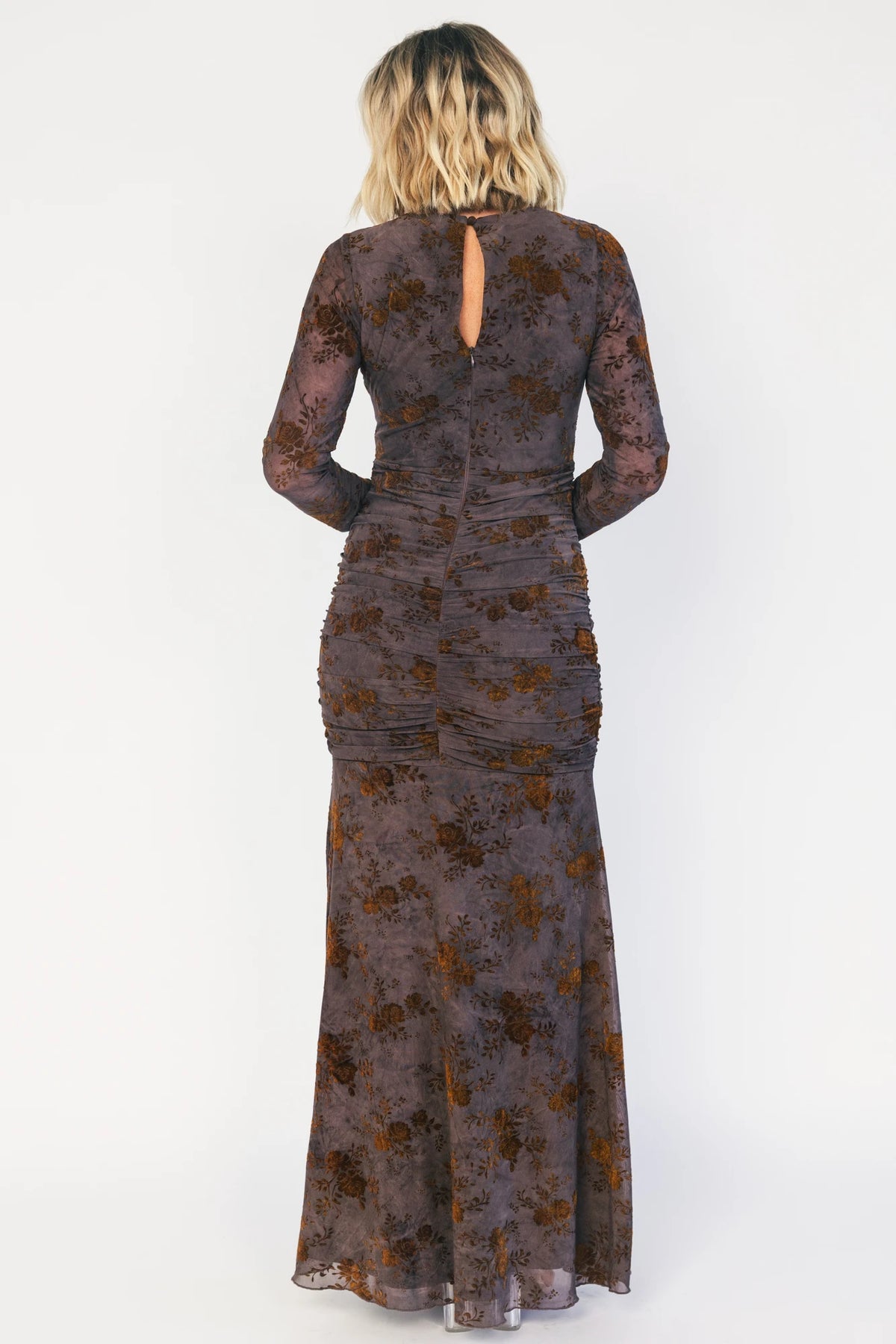 Model wearing a clove maxi dress with copper velvet burnout detailing, a high round neckline, and long sheer sleeves.
