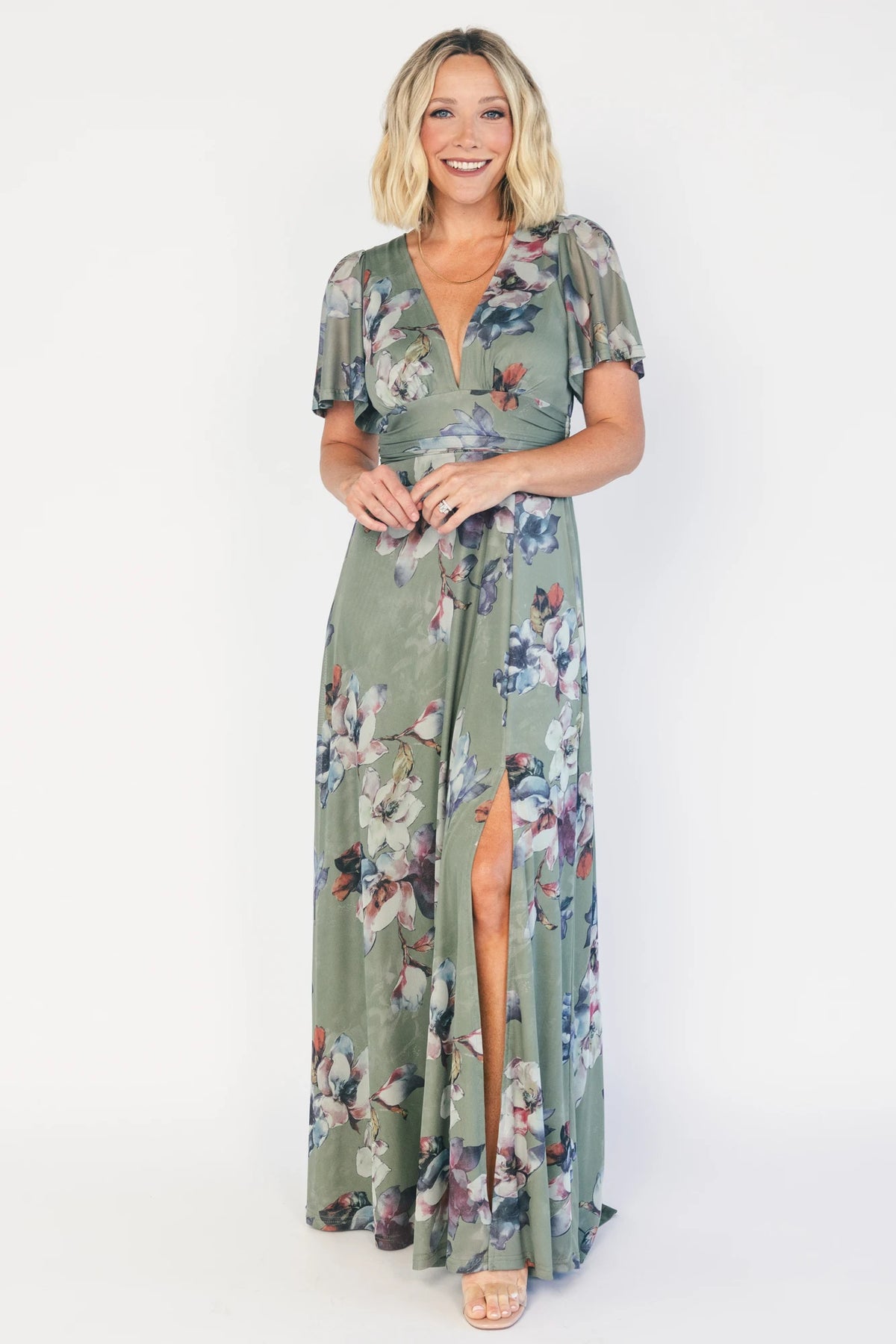 Model wearing a sage floral maxi dress with a deep V-neckline, short flutter sleeves, and an empire waist.