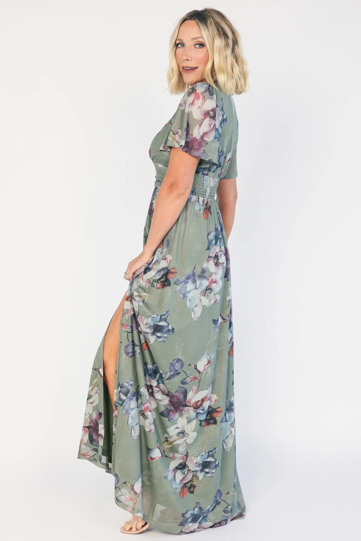 Model wearing a sage floral maxi dress with a deep V-neckline, short flutter sleeves, and an empire waist.