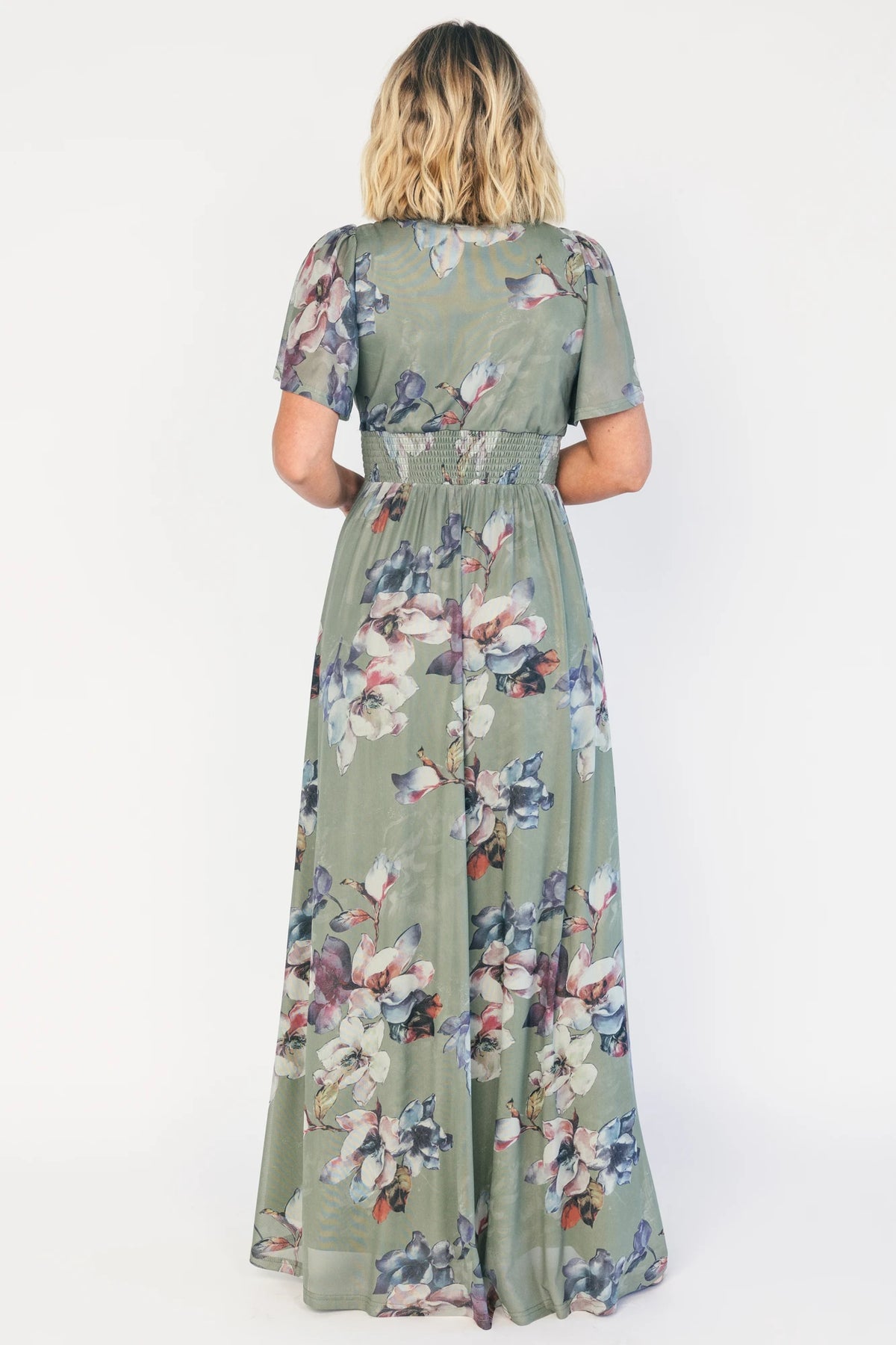 Model wearing a sage floral maxi dress with a deep V-neckline, short flutter sleeves, and an empire waist.
