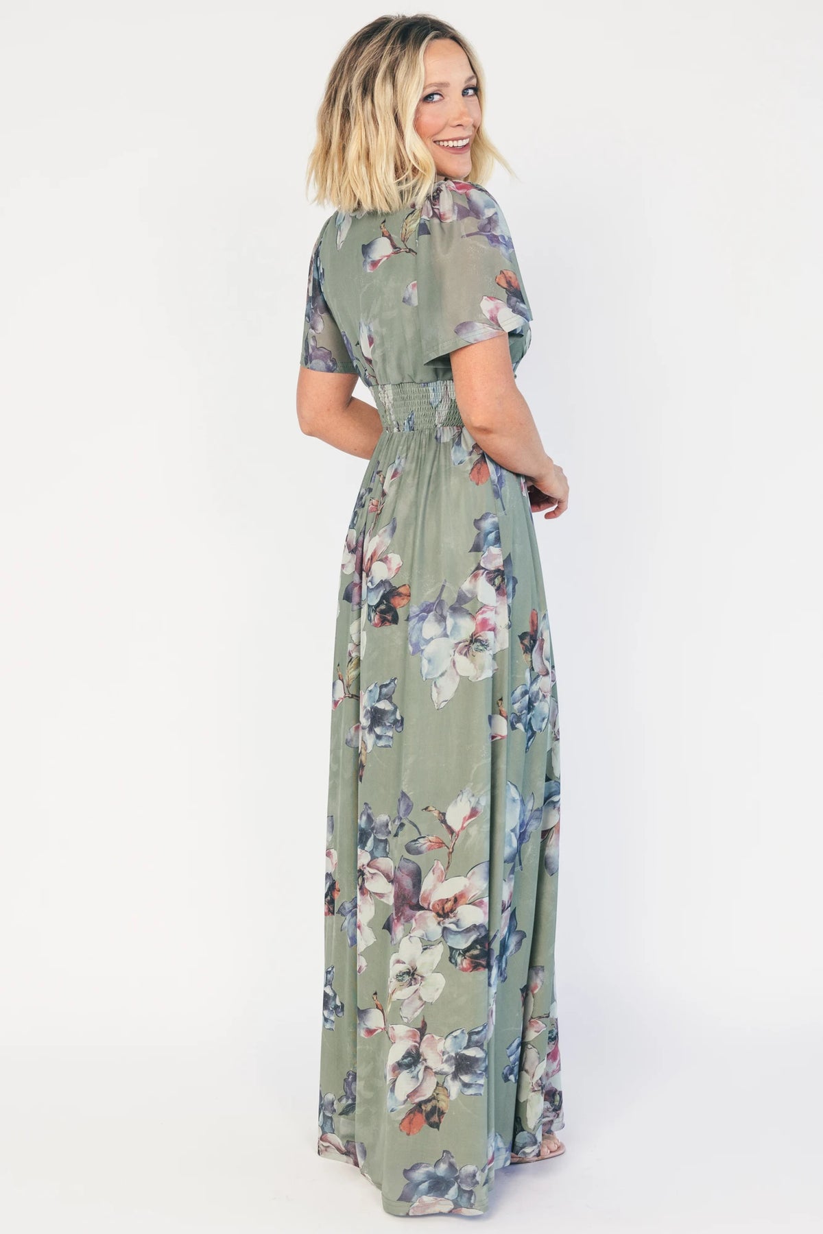 Model wearing a sage floral maxi dress with a deep V-neckline, short flutter sleeves, and an empire waist.