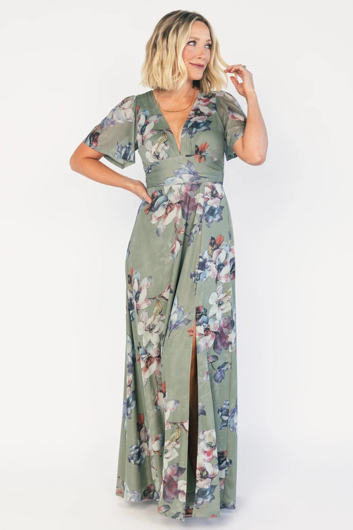 Model wearing a sage floral maxi dress with a deep V-neckline, short flutter sleeves, and an empire waist.