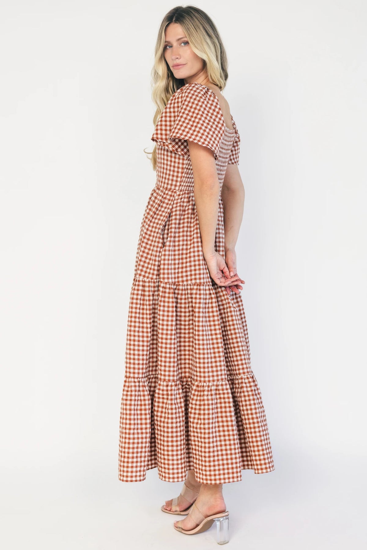 Model wearing a spice and white gingham maxi dress with a square neckline, flutter sleeves, and a fitted bodice with a smocked back