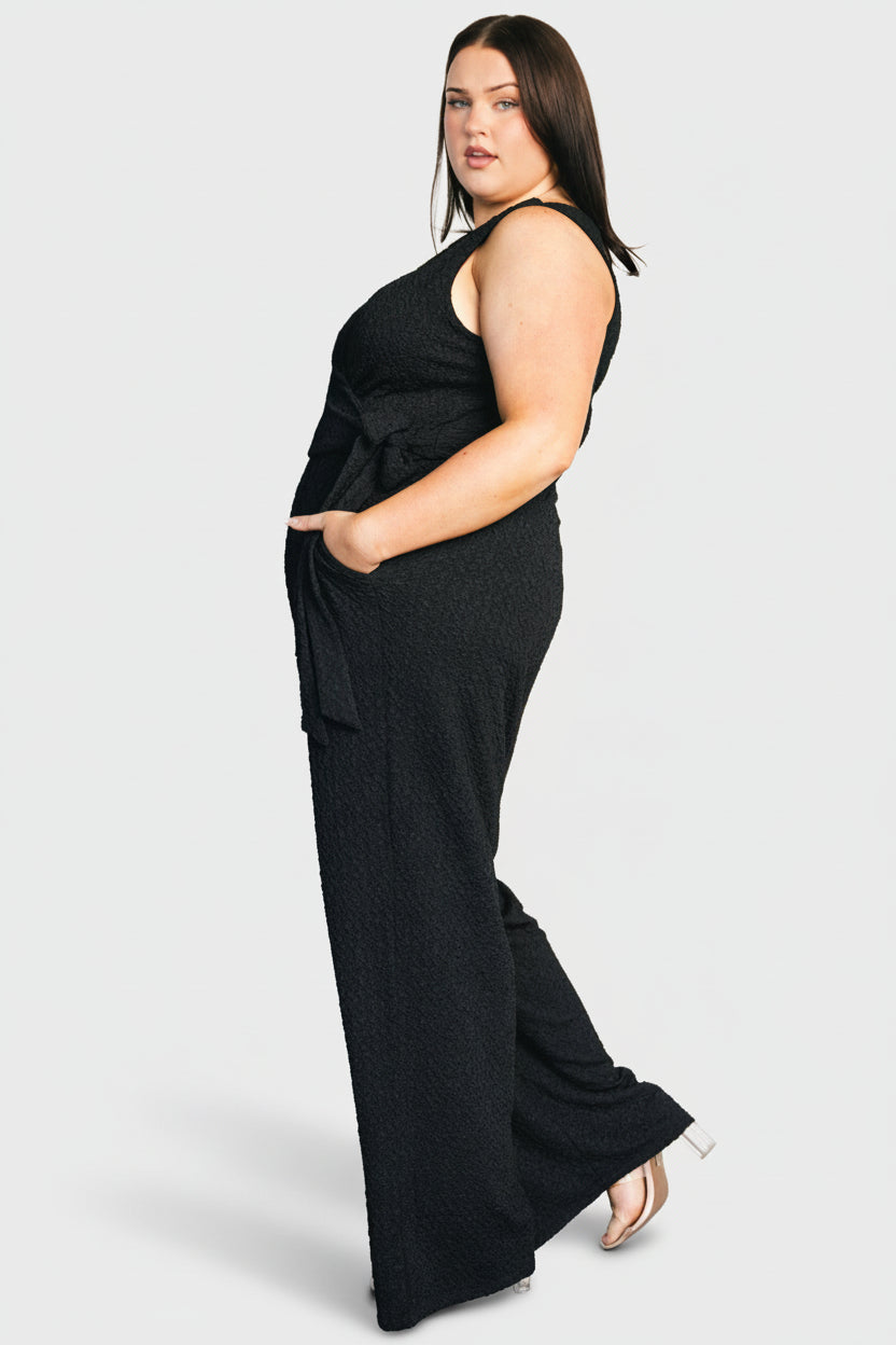 Studio full-length back and side view of Natasha Jumpsuit in black, highlighting elastic waistband and wide-leg hem.