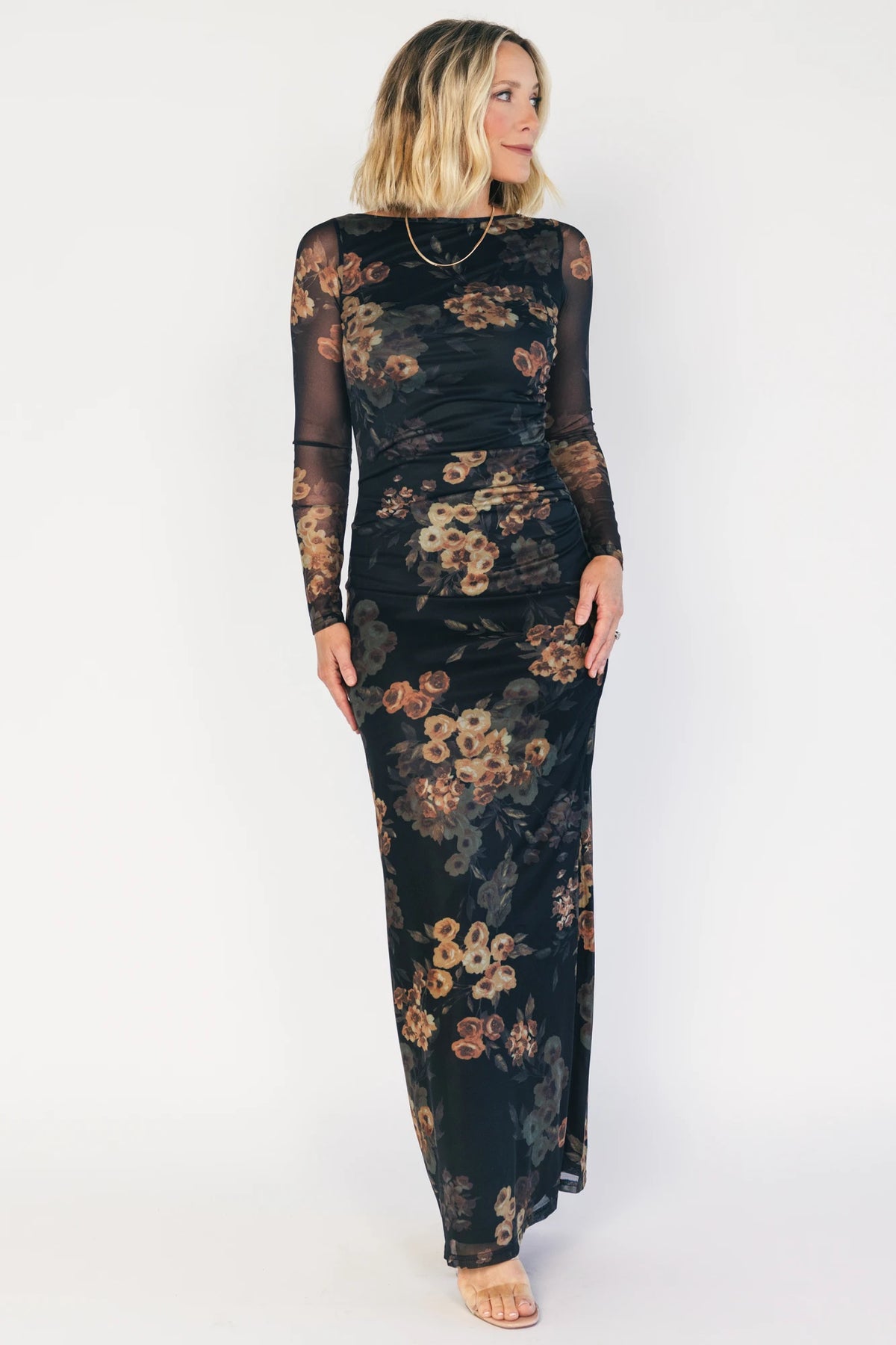Black mesh bodycon midi dress with muted gold floral print, sheer long sleeves, a round neckline, flattering side ruching, and a thigh-high side slit.