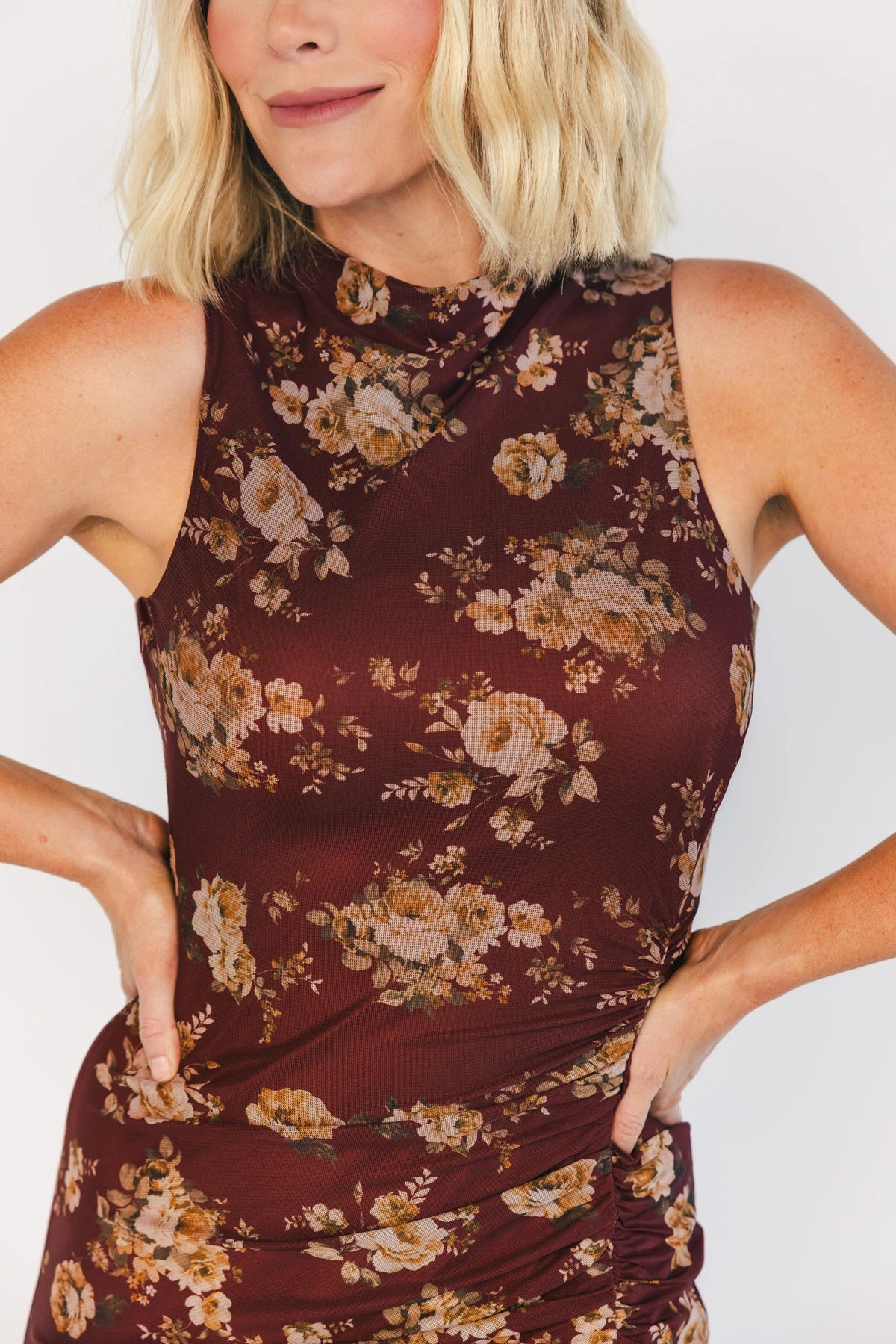 Model wearing a mahogany floral maxi dress with a high neckline, sleeveless fitted bodice, and ruched side detailing.
