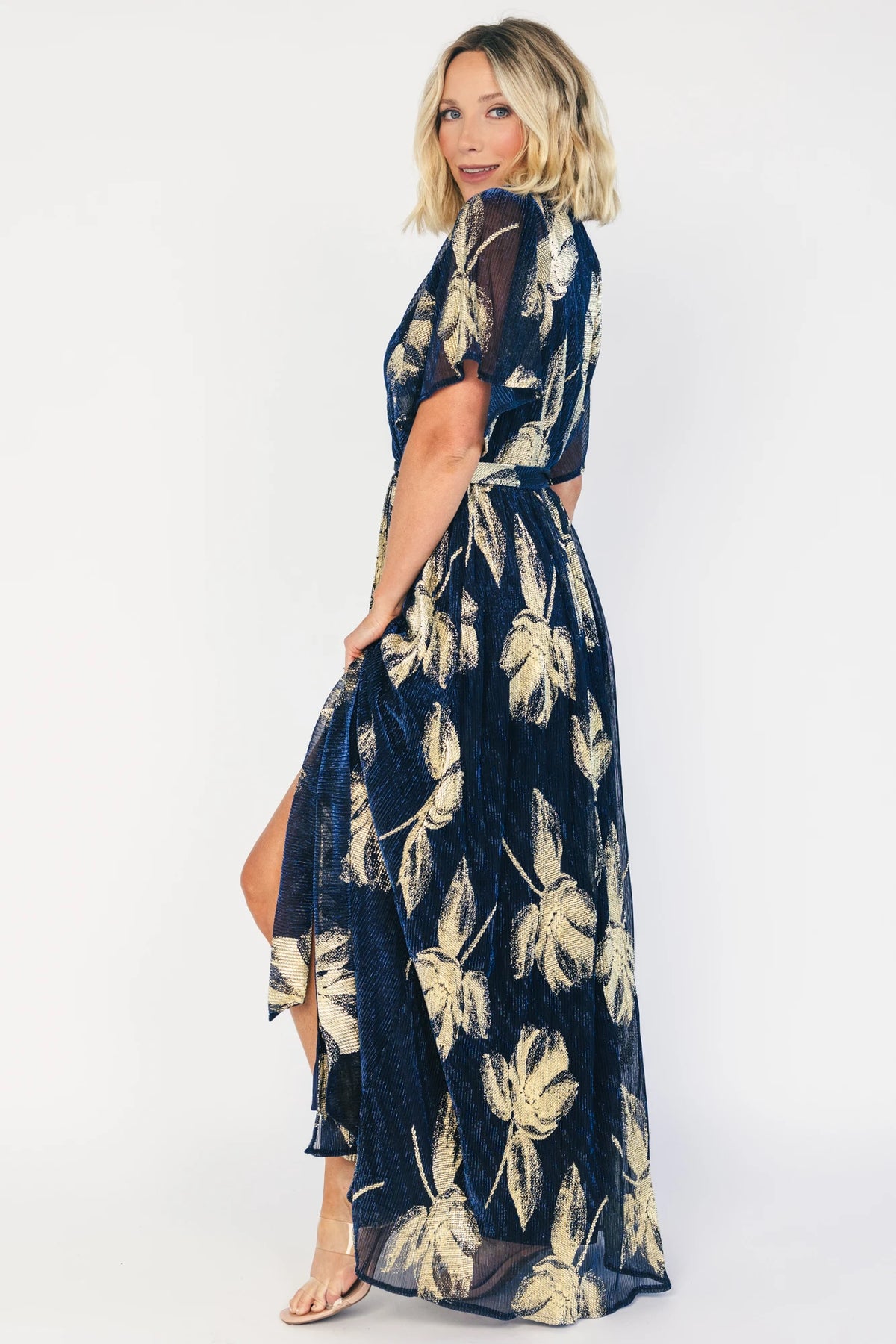 Rachel Maxi Dress in Navy + Gold with shimmer finish, surplice neckline, self-tie sash, long sleeves, and leg slit.