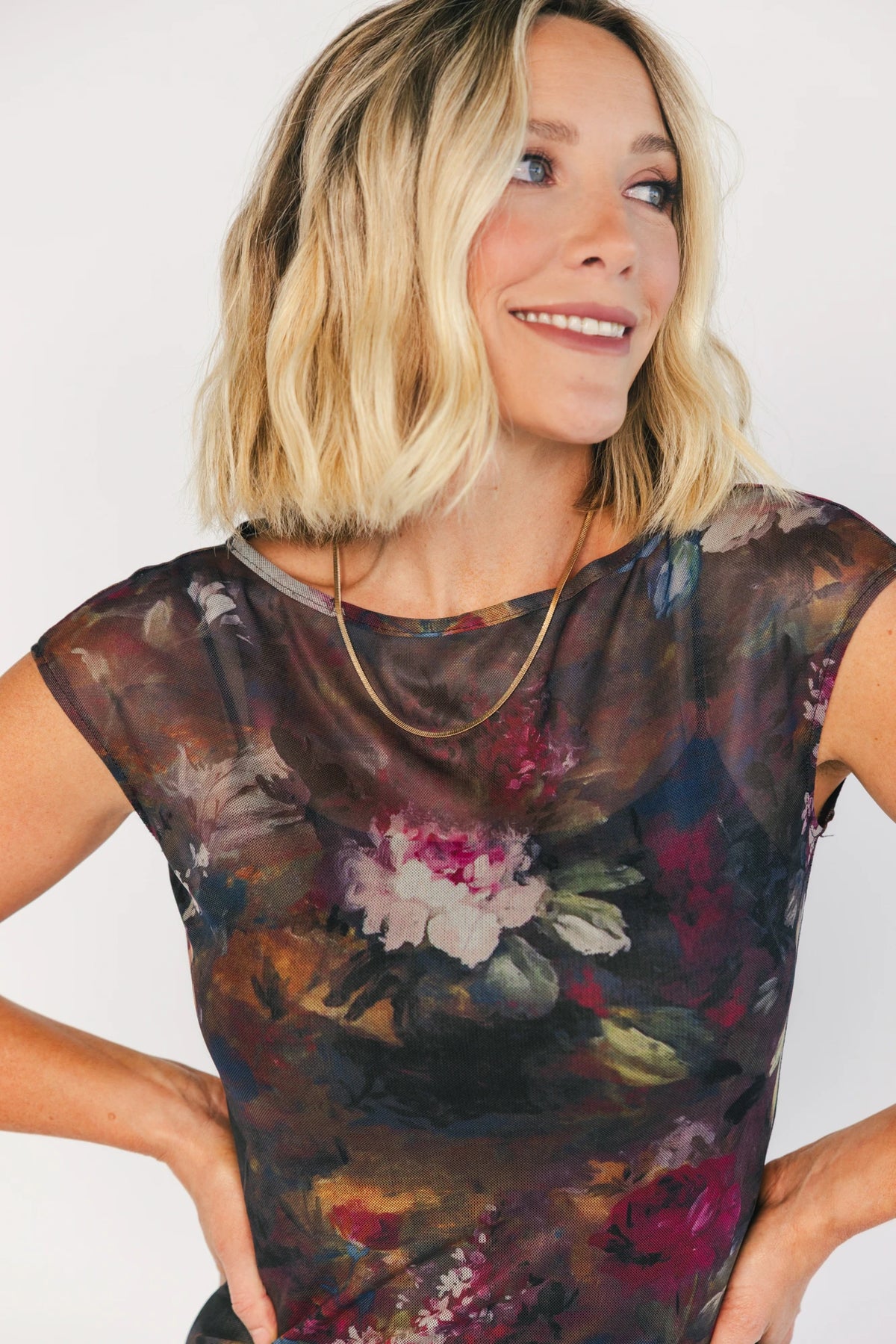 Model wearing the Daniela Mesh Midi Dress in Brown Floral, a fitted mesh midi dress with a brown floral print, round neckline, short sleeves, and a bodycon silhouette layered over a ribbed slip.