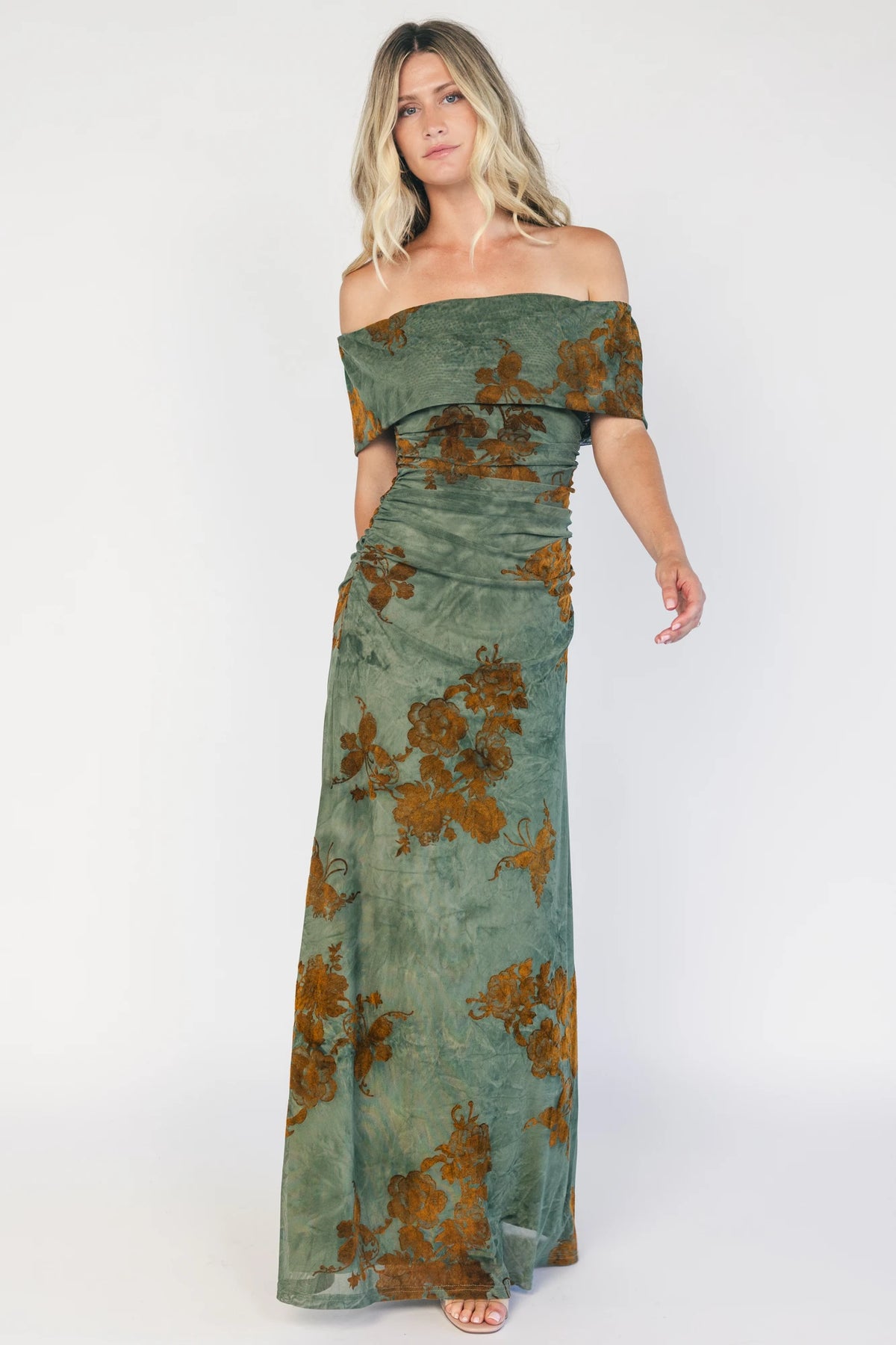 Model wearing an off-the-shoulder maxi dress with a green mesh overlay and copper velvet floral detailing.