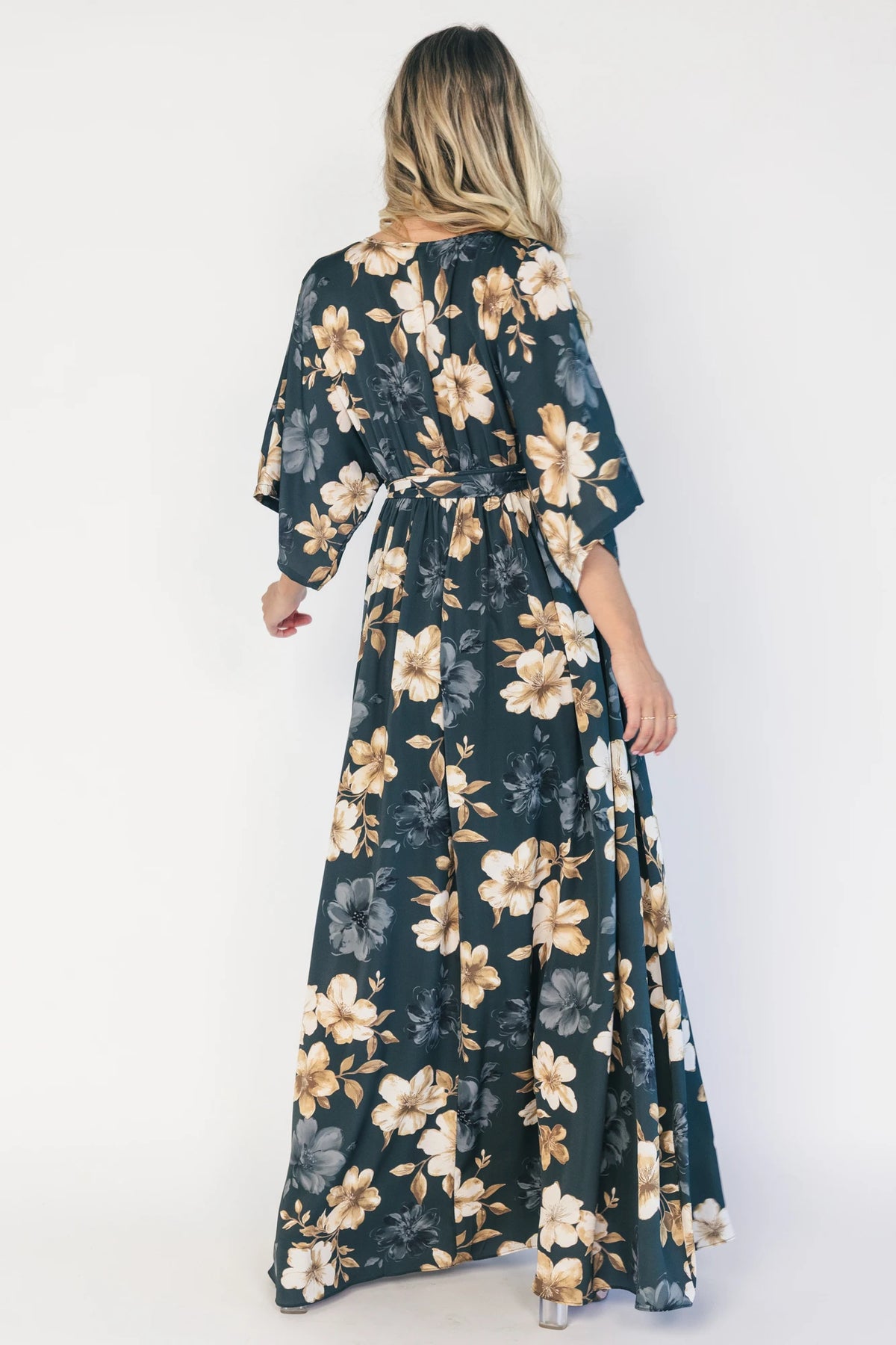 Model wearing a dark jade floral maxi dress with a surplice V-neckline, kimono sleeves, and an elastic waist with a removable sash tie.