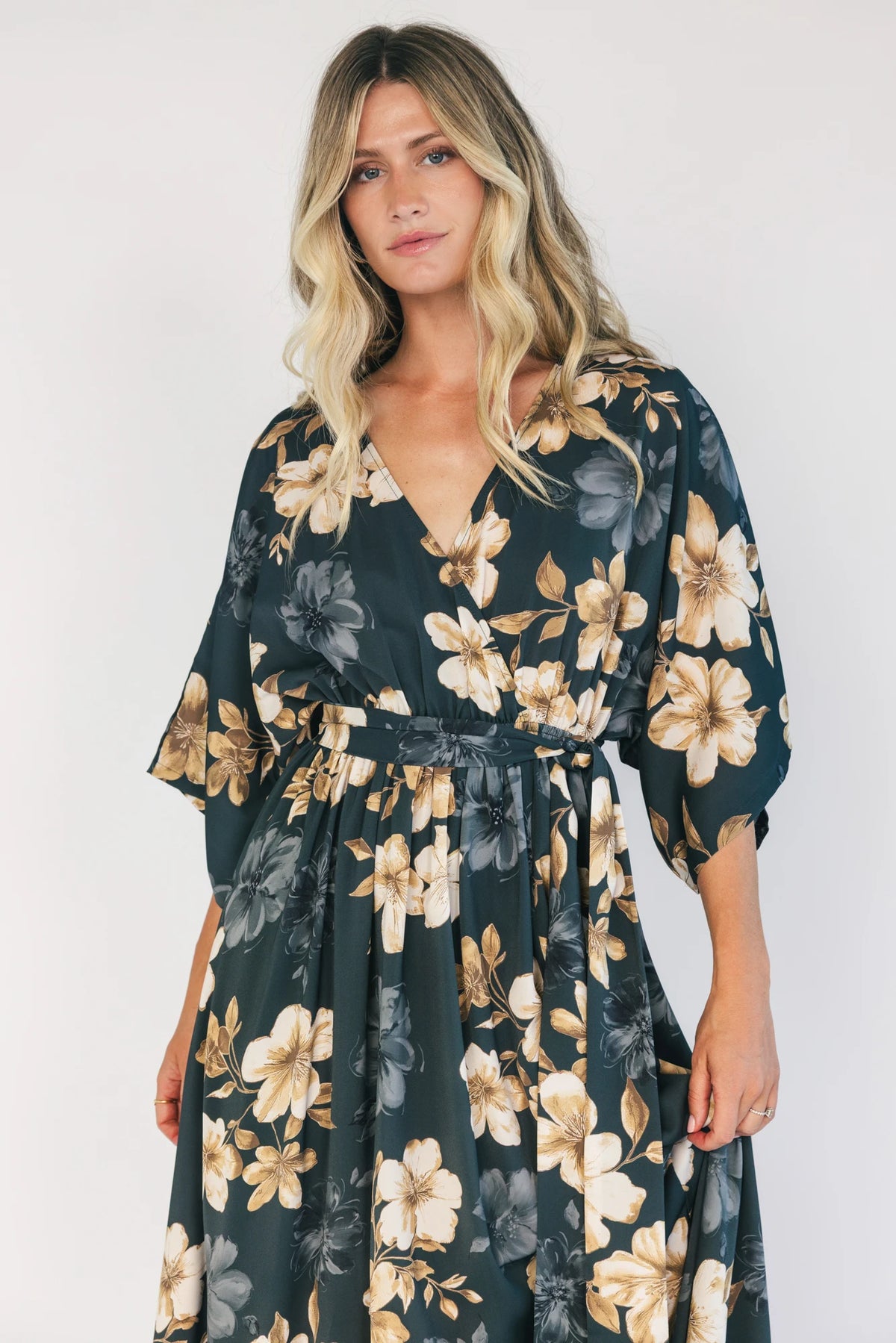 Model wearing a dark jade floral maxi dress with a surplice V-neckline, kimono sleeves, and an elastic waist with a removable sash tie.