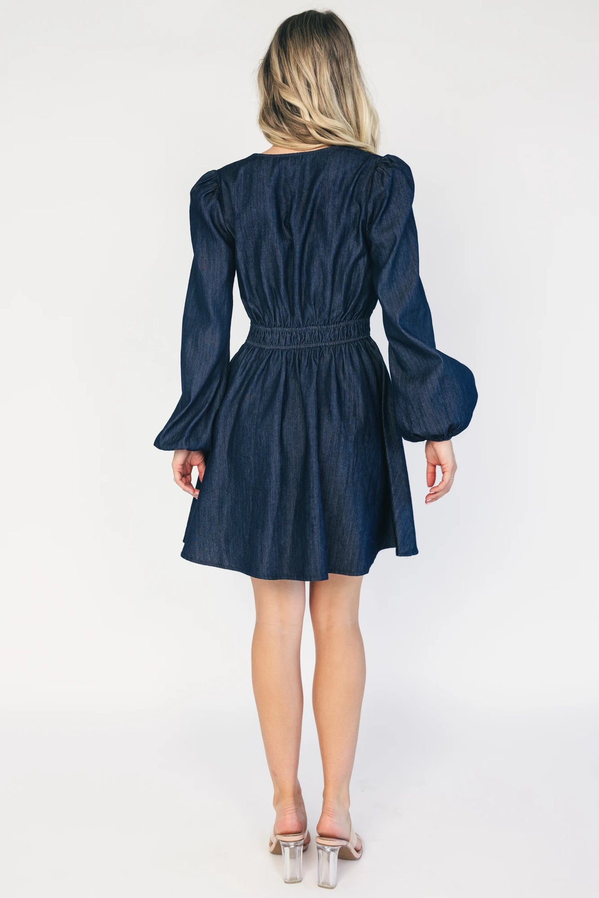 Model wearing a dark chambray short dress with a V-neckline, floral embroidery at the bust, long sleeves with elastic cuffs, and a double elastic waistband.