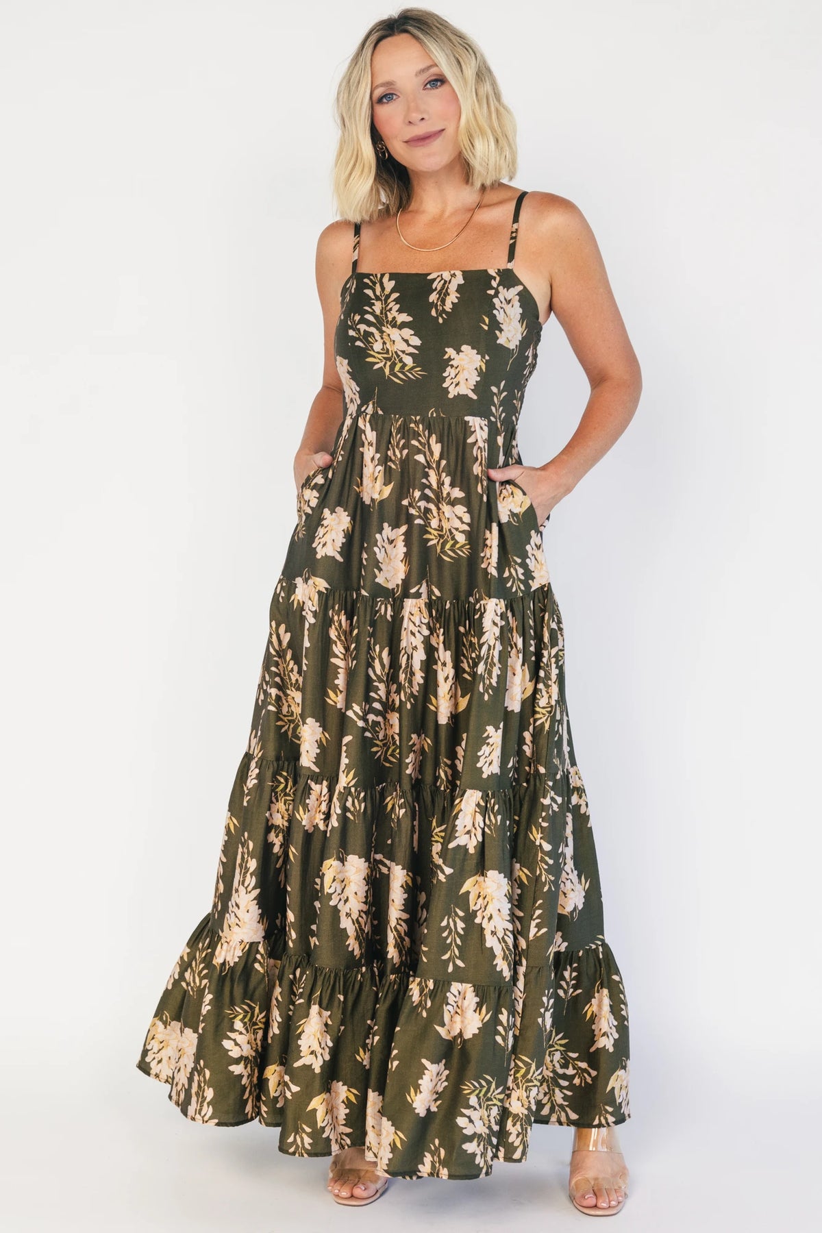Model wearing an olive floral maxi dress with a square neckline, adjustable spaghetti straps, and a smocked back bodice.