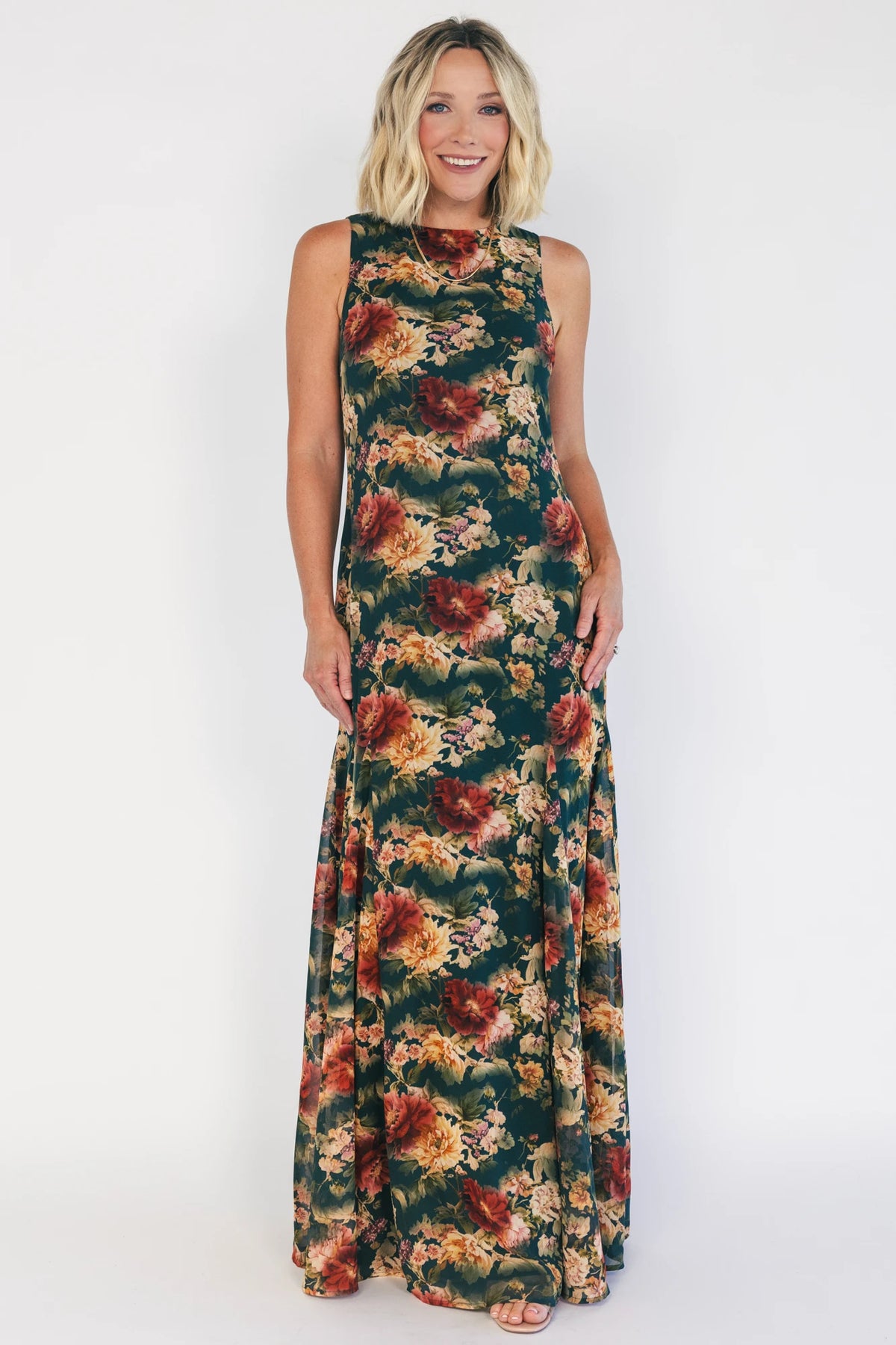 Model wearing a topaz floral maxi dress with a high round neckline, sleeveless bodice, and an open back with a sash tie.
