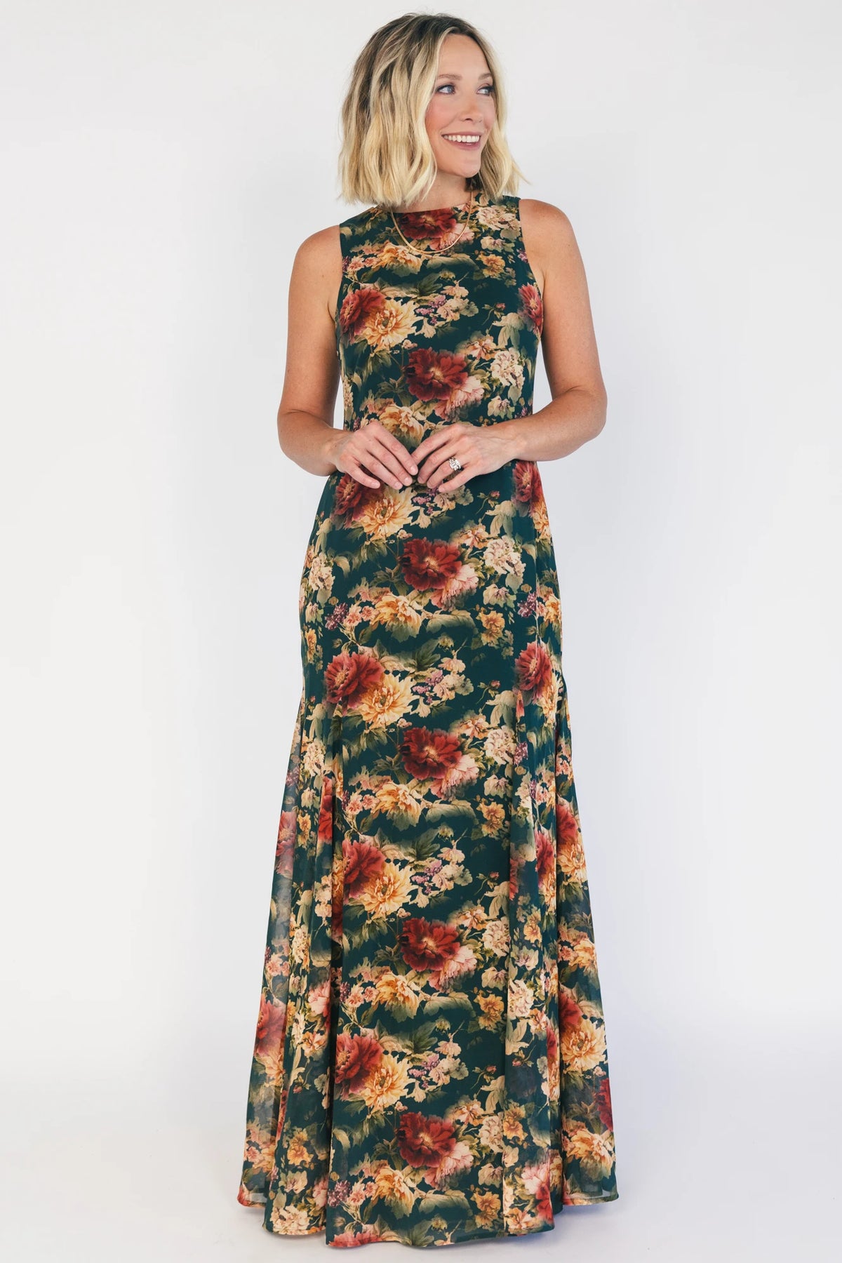 Model wearing a topaz floral maxi dress with a high round neckline, sleeveless bodice, and an open back with a sash tie.