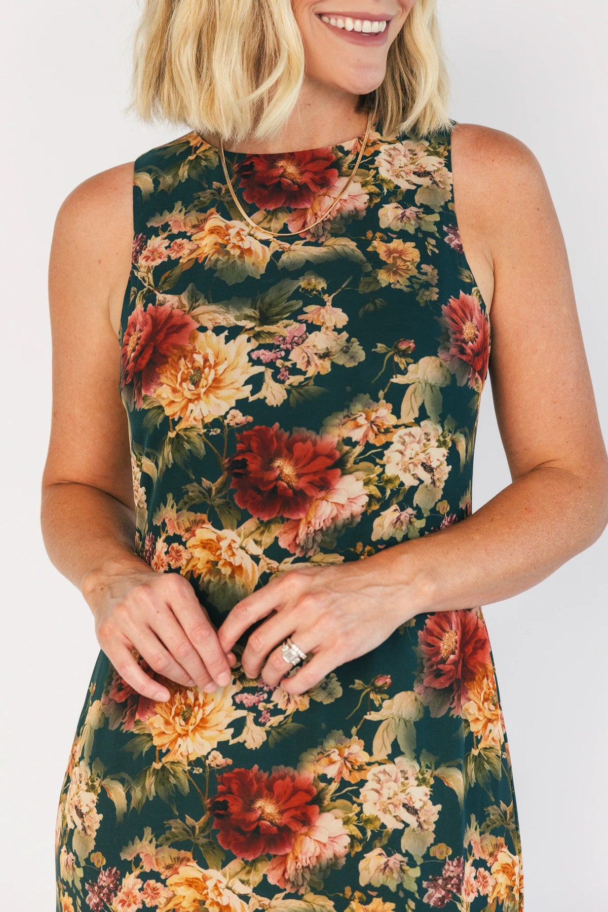 Model wearing a topaz floral maxi dress with a high round neckline, sleeveless bodice, and an open back with a sash tie.