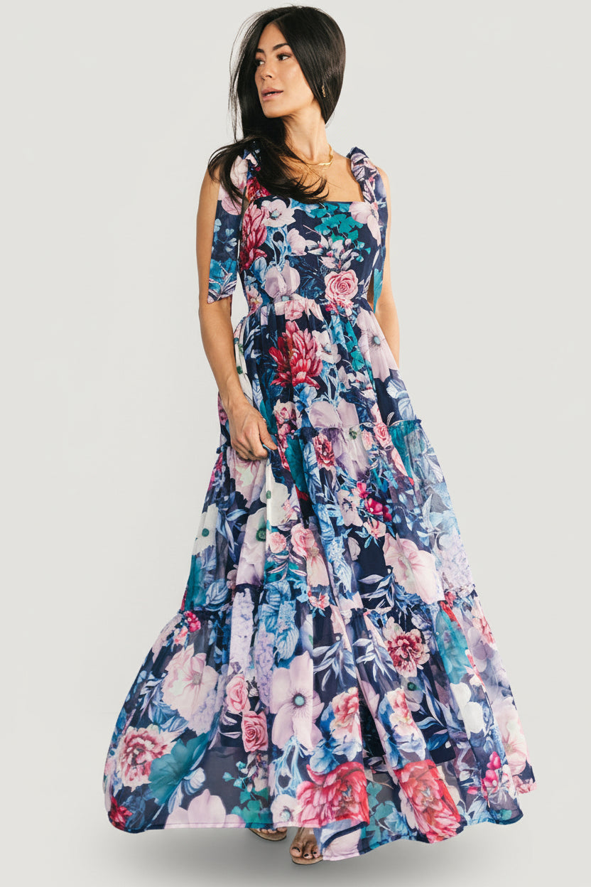 Front view of Anita Maxi Dress in dark blue with pink and blue floral print, square neckline, adjustable self-tie straps, and three ruffled tiers.