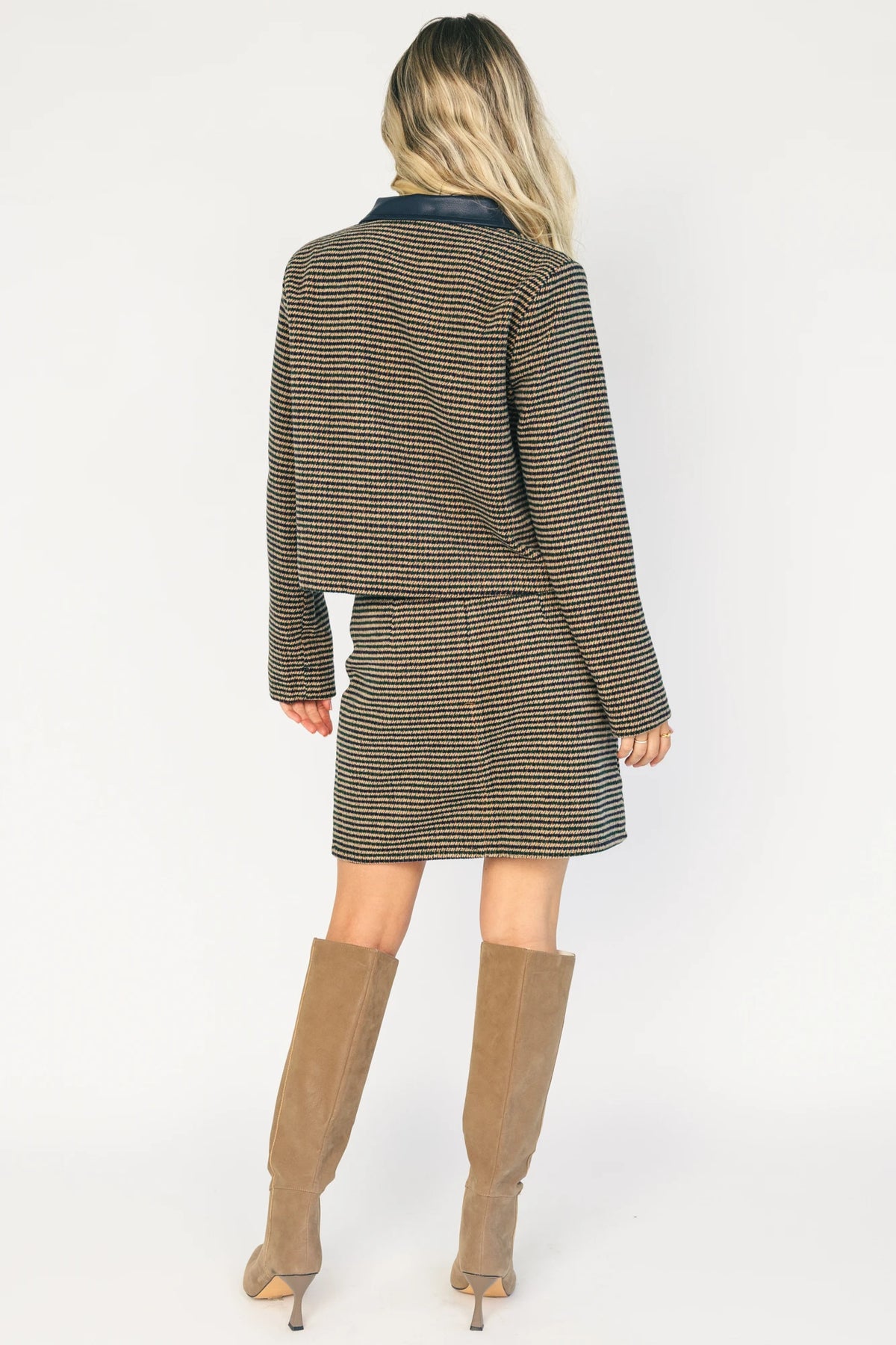 Model wearing the Gracey Set in Navy + Tan featuring a navy and tan striped tweed jacket with a collared neckline, faux leather trim, button-front closure, and matching mini skirt for a polished, coordinated look.
