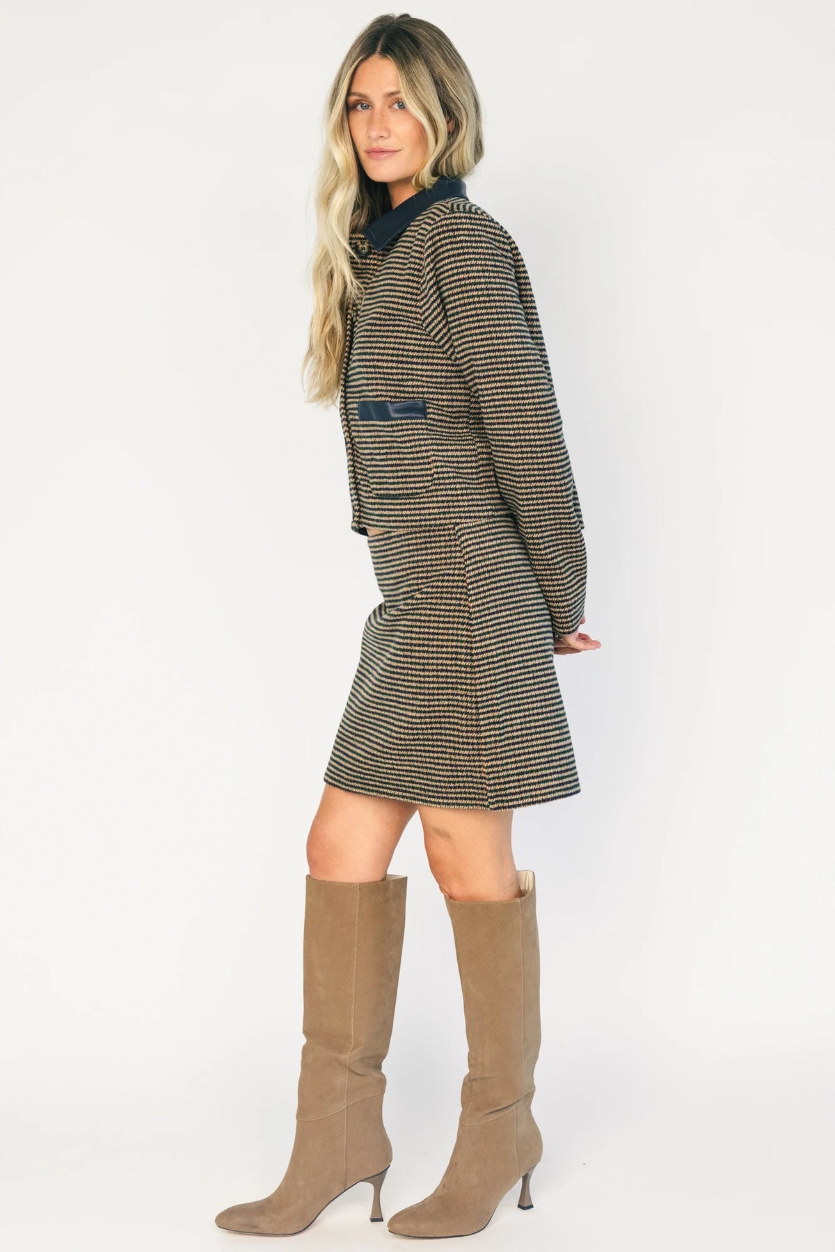 Model wearing the Gracey Set in Navy + Tan featuring a navy and tan striped tweed jacket with a collared neckline, faux leather trim, button-front closure, and matching mini skirt for a polished, coordinated look.