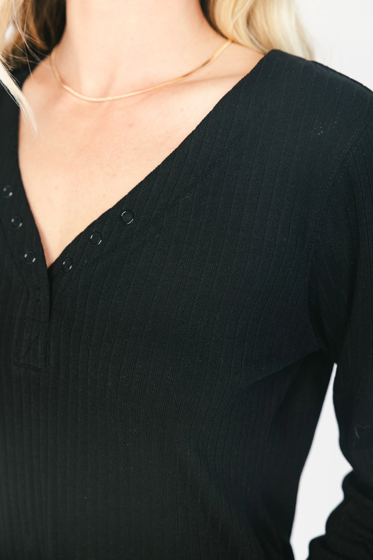 Model wearing the Rubi Soft Ribbed Pajama Set in Black featuring a soft ribbed knit, long-sleeve V-neck top with a snap-button placket, and matching straight-leg pants with an elastic waistband and side pockets.