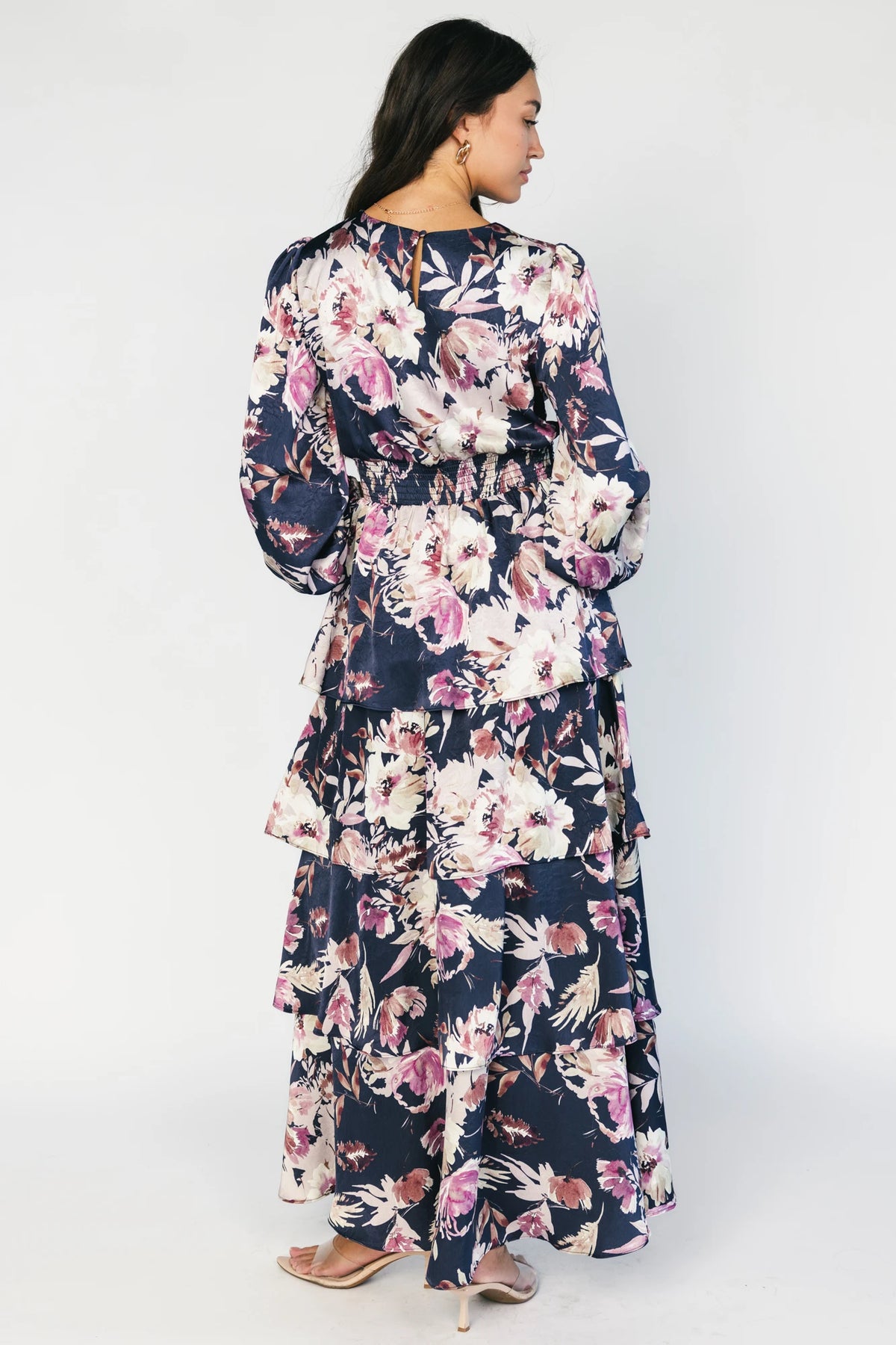 Model wearing the Montrouge Tiered Satin Maxi Dress in Navy + Lilac Floral featuring a V-neckline, short flutter sleeves, a smocked back, and a flowing tiered satin maxi skirt with a navy background and lilac floral print.