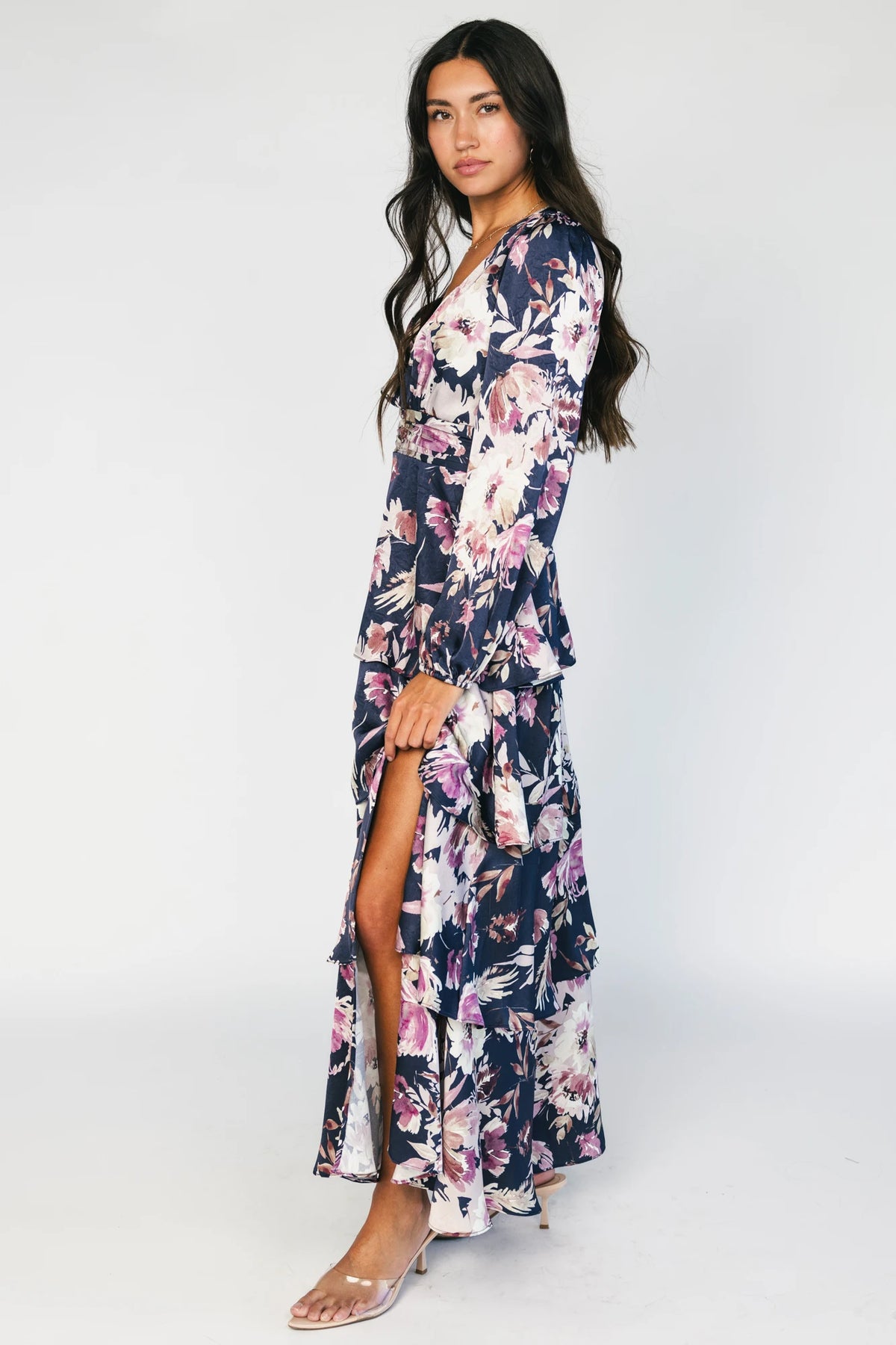 Model wearing the Montrouge Tiered Satin Maxi Dress in Navy + Lilac Floral featuring a V-neckline, short flutter sleeves, a smocked back, and a flowing tiered satin maxi skirt with a navy background and lilac floral print.