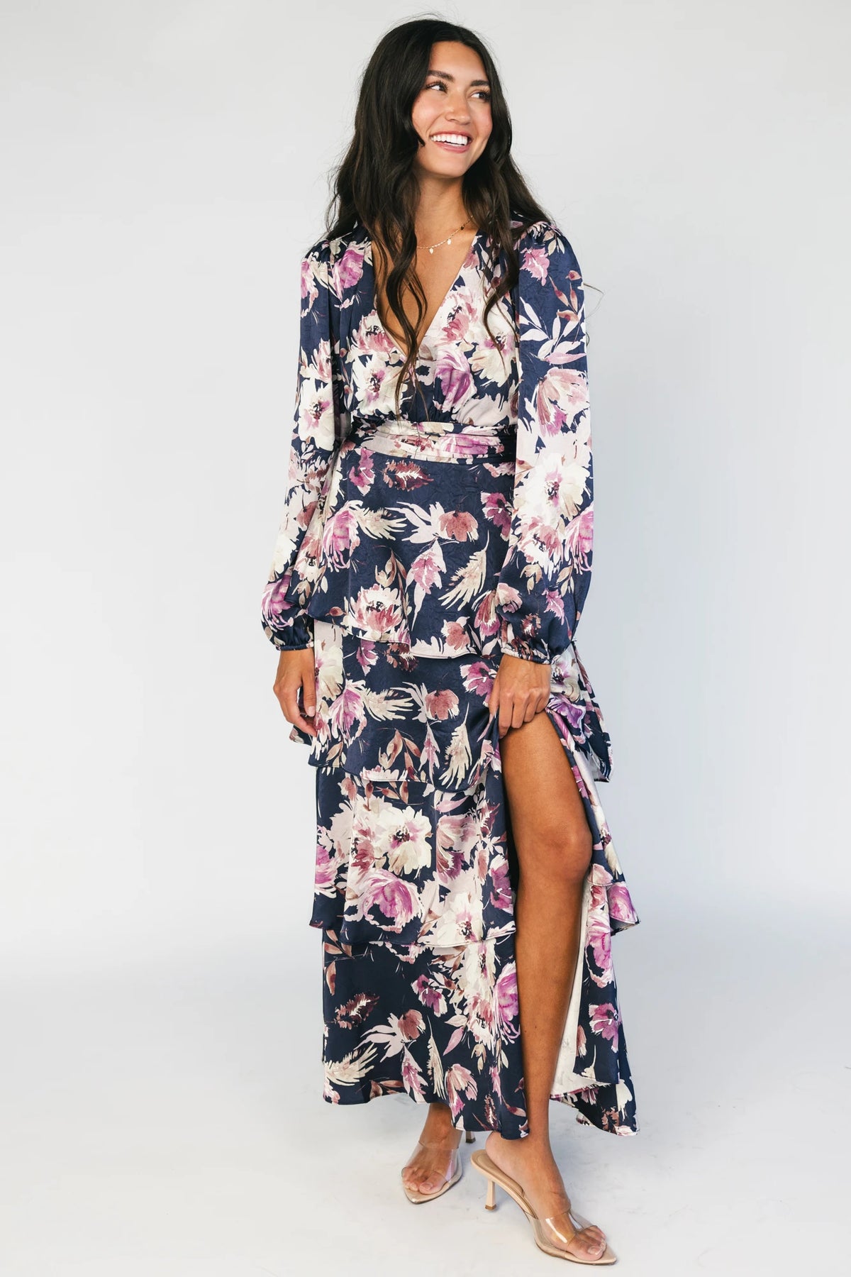 Model wearing the Montrouge Tiered Satin Maxi Dress in Navy + Lilac Floral featuring a V-neckline, short flutter sleeves, a smocked back, and a flowing tiered satin maxi skirt with a navy background and lilac floral print.