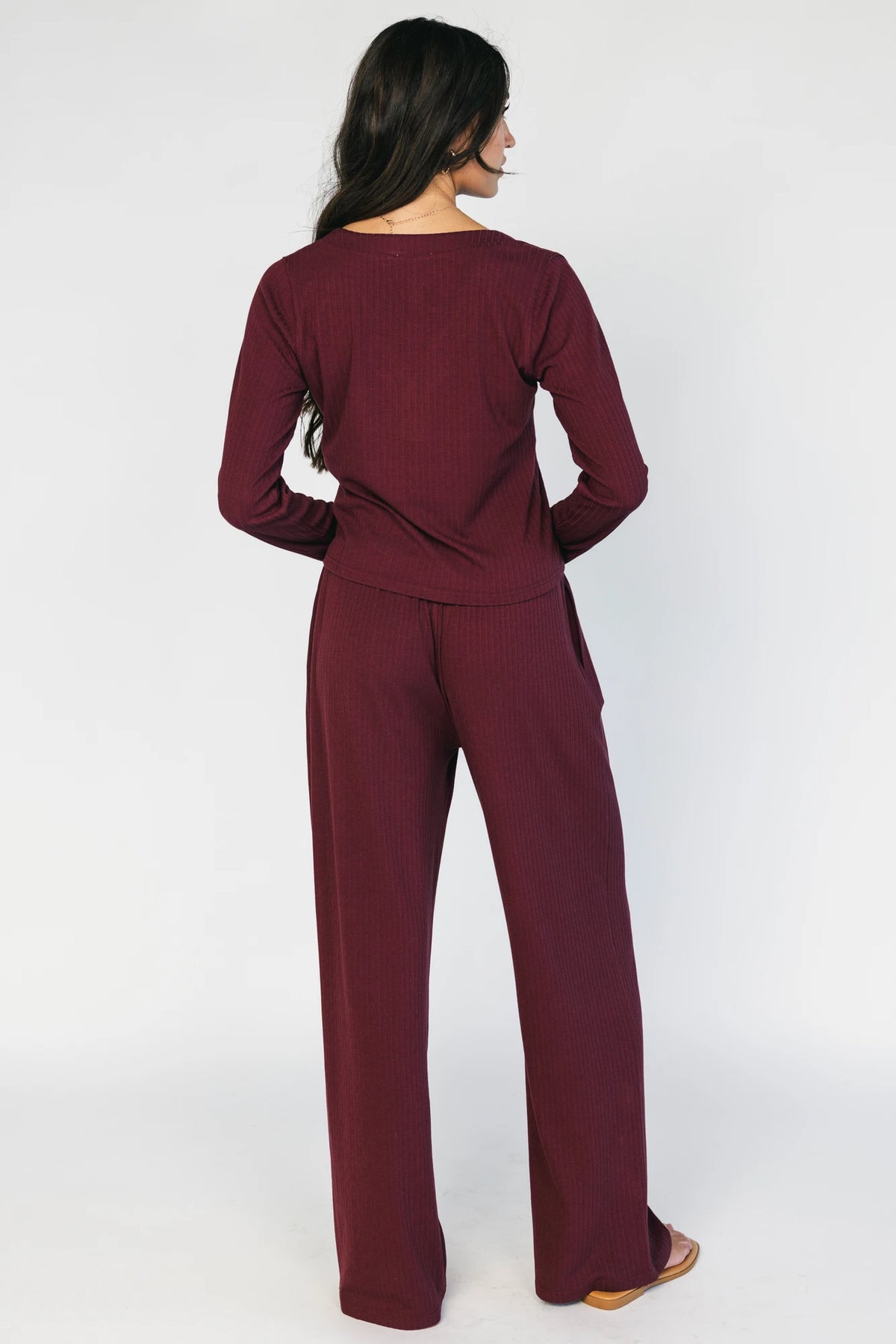 Model wearing the Rubi Soft Ribbed Pajama Set in Burgundy featuring a soft ribbed knit, long-sleeve V-neck top with a snap-button placket, and matching straight-leg pants with an elastic waistband and side pockets.
