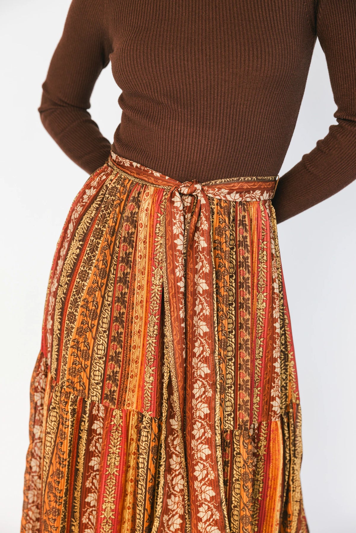 Brown ribbed sweater maxi dress with long sleeves, a high round neckline, removable waist tie, and a flowing multicolor chiffon skirt.