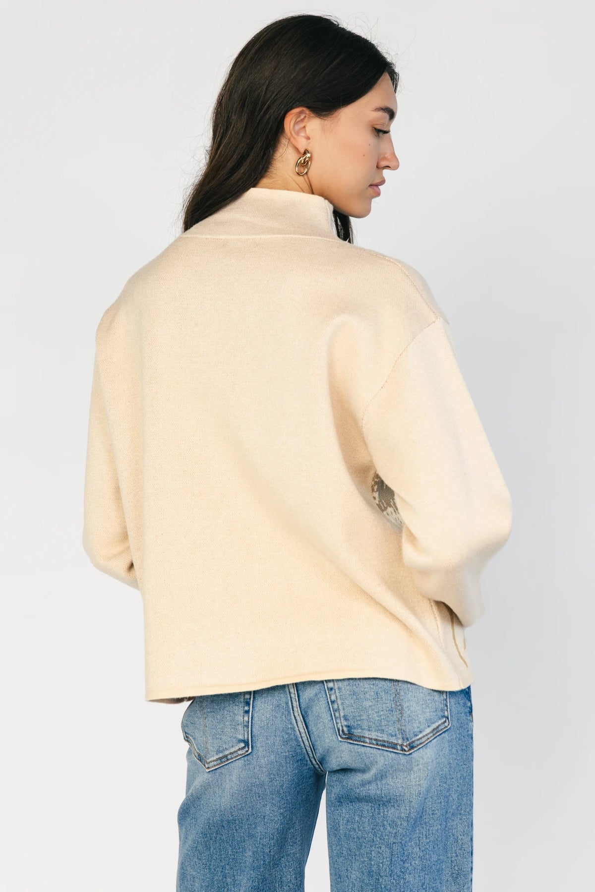 Natural knit sweater with a mock neckline, long sleeves, relaxed fit, and an embroidered floral motif at the neckline.