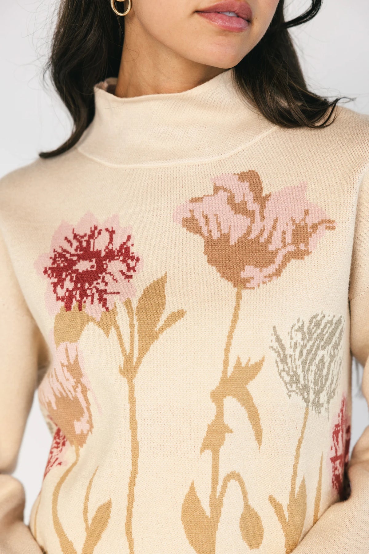 Natural knit sweater with a mock neckline, long sleeves, relaxed fit, and an embroidered floral motif at the neckline.