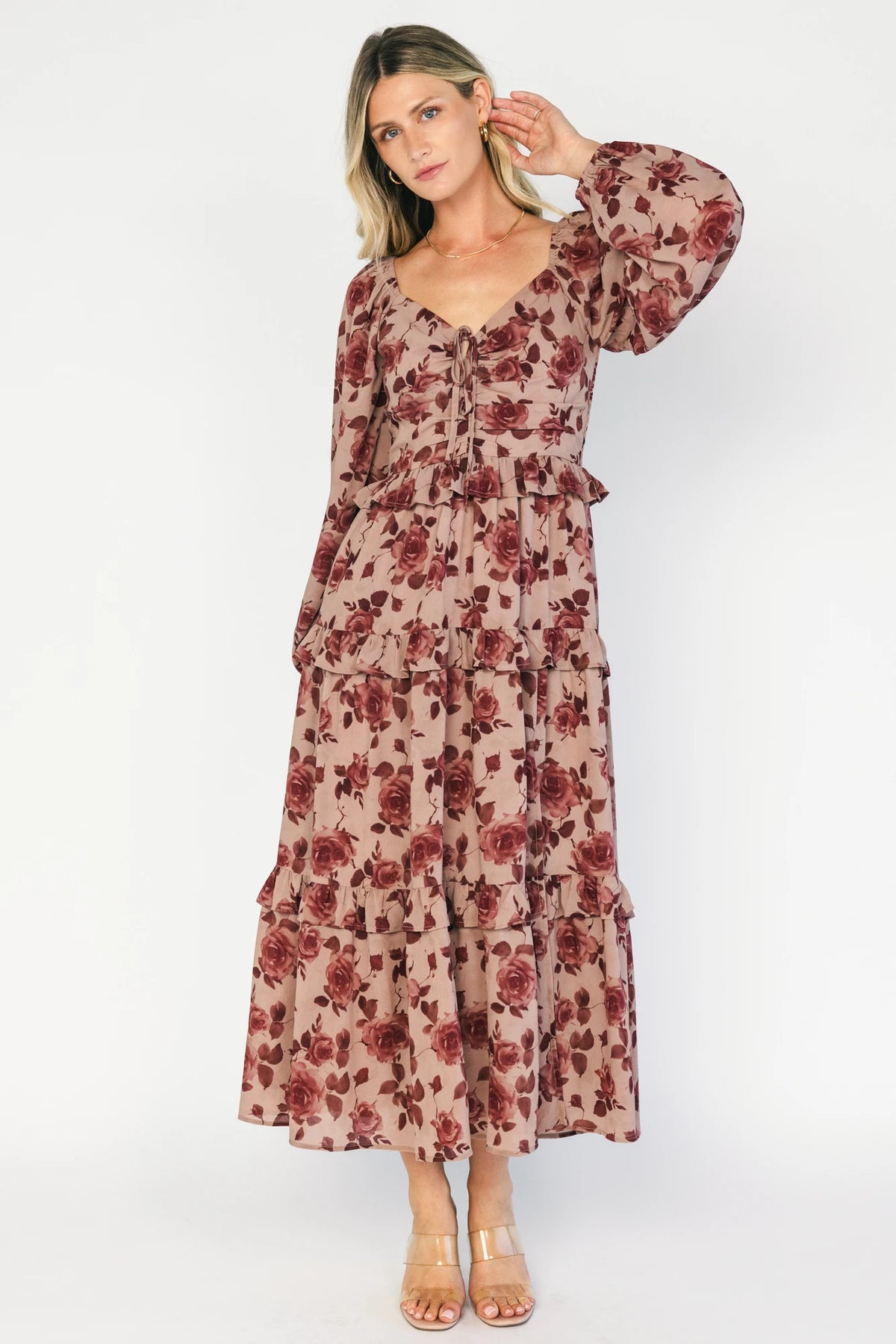 Model wearing a dusty mauve floral maxi dress with a sweetheart neckline, adjustable tie-front bust, and long sheer sleeves.