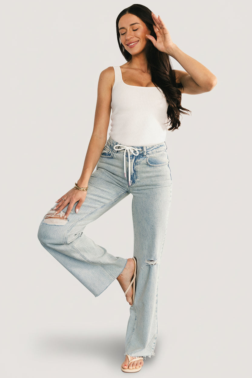 Flatlay of Ronda mid-rise ripped jeans in light wash, displaying front distressing, drawstring details and raw frayed hem for product overview.