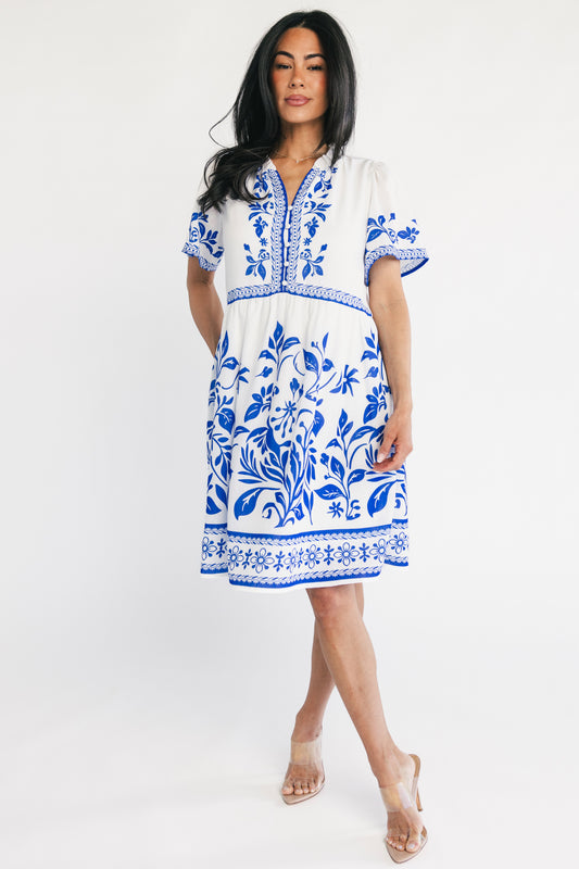 White short dress with cobalt-blue floral print, notched ruffle neckline, button-front, short sleeves and side pockets.